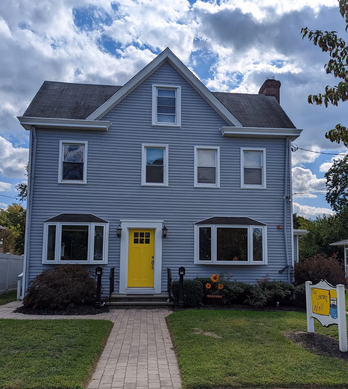 Blue, two-story building with a bright yellow front door and a Learning Well sign.