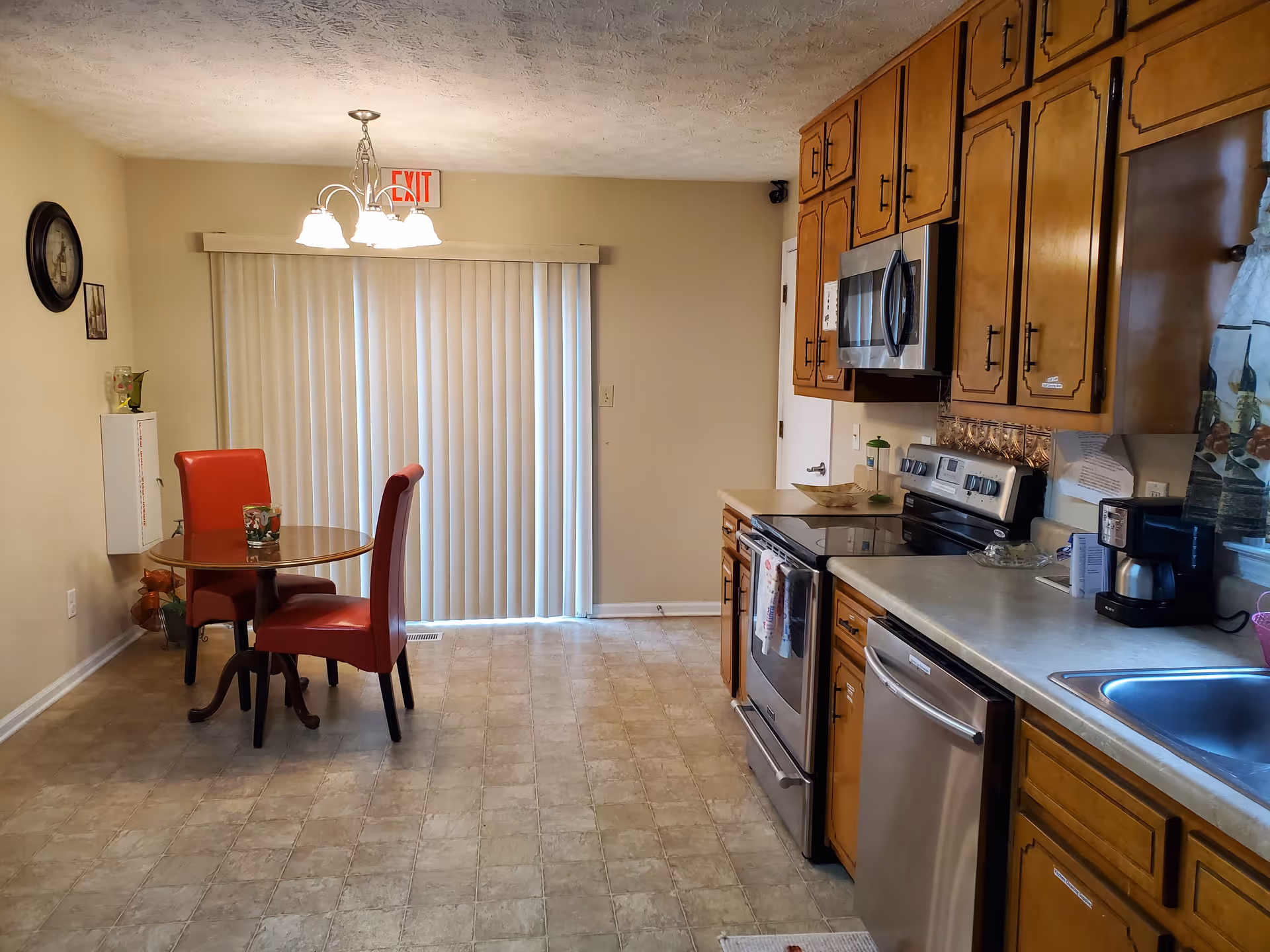 Senior living facility kitchen with wooden cabinets, stainless appliances, and red chairs.