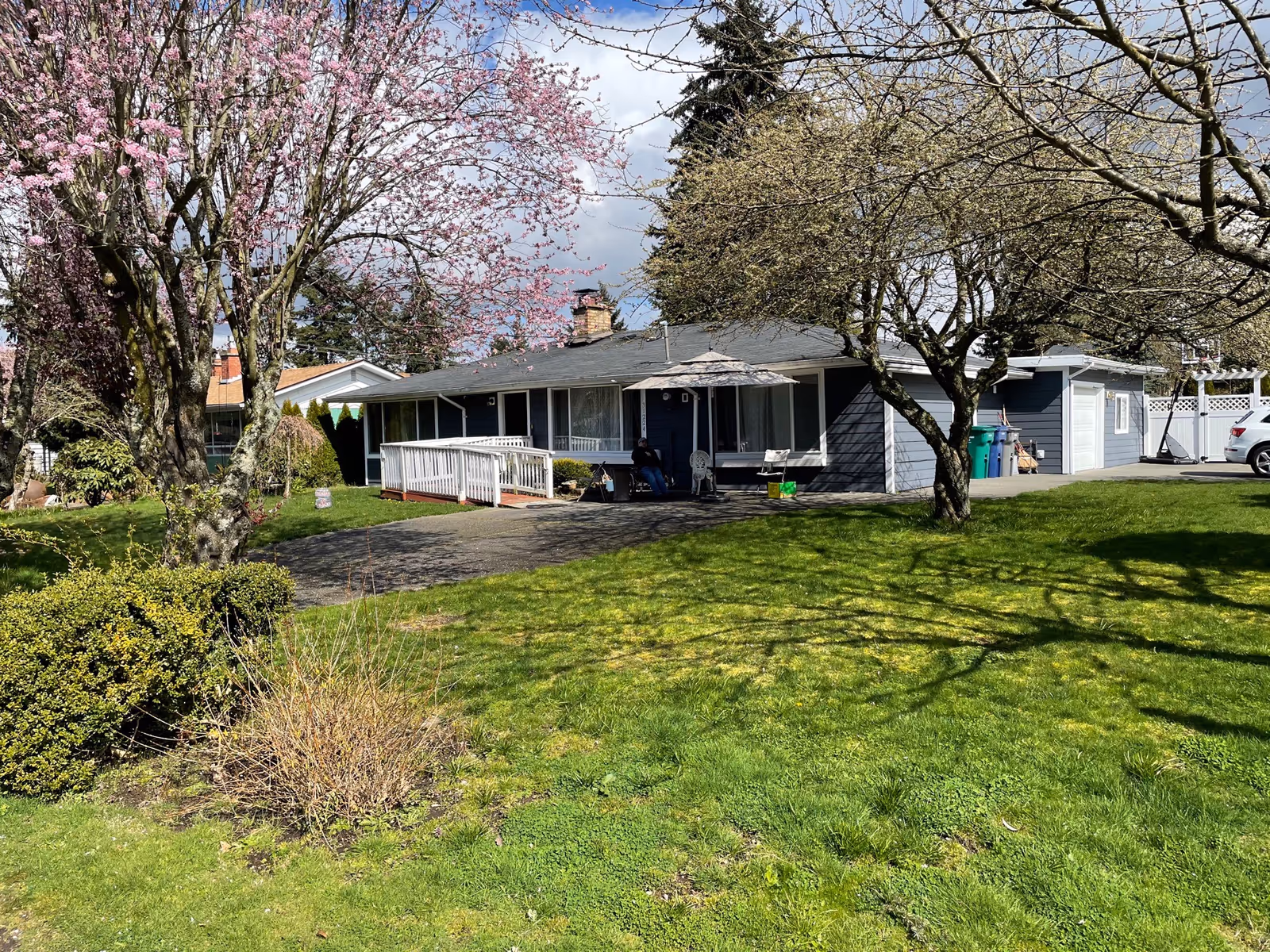 Front exterior of Alpine Heritage facility with blossoming trees, ramp, and driveway.