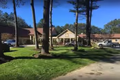 Exterior view of Alpine Nursing Home, a single-story brick building with a front entrance and cars.