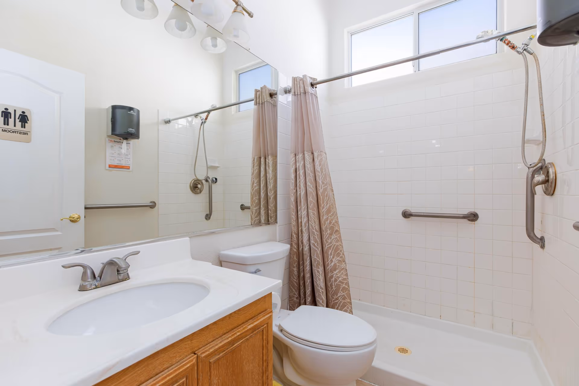 Bright bathroom with sink, toilet, walk-in shower, and accessible grab bars.
