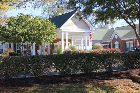Front view of Windsor Gardens Senior Living building with porch, American flag, and shrubs.