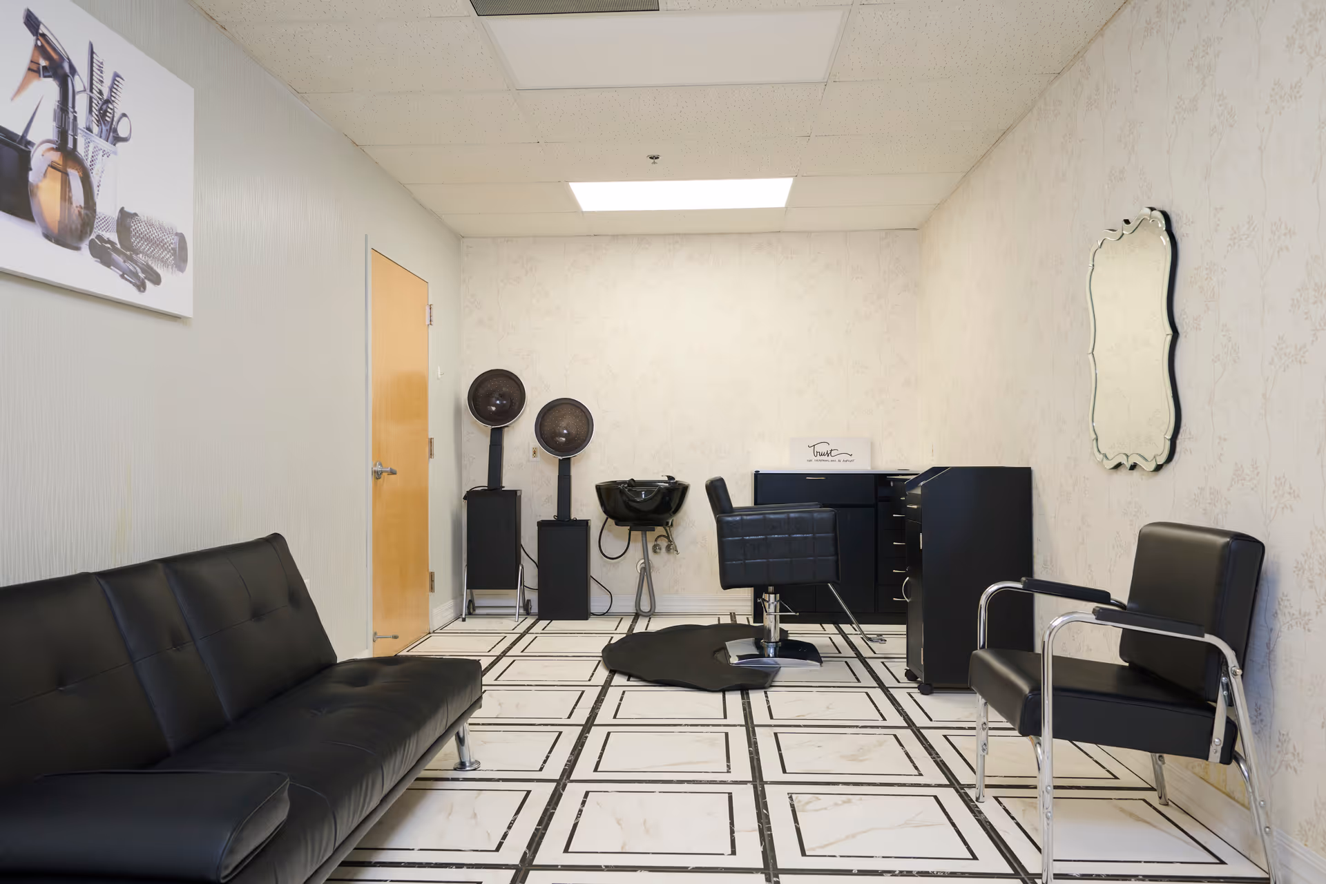 Interior salon area with black seating, styling chair, mirror, and hair equipment.