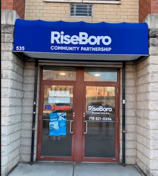 Blue awning with RiseBoro Community Partnership over glass doors at building entrance.