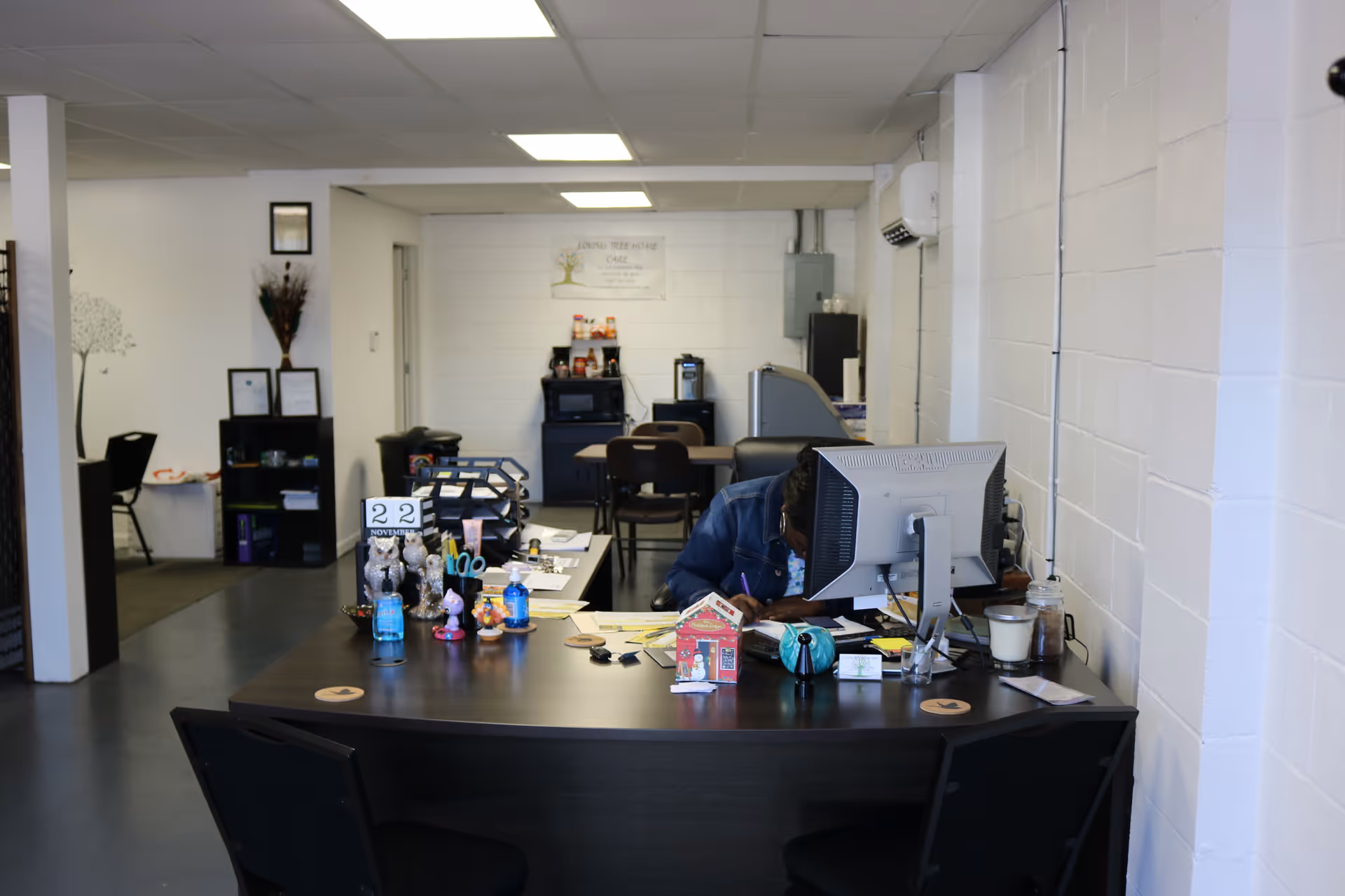 Office reception area with a desk, computer, and a staff member inside a facility.
