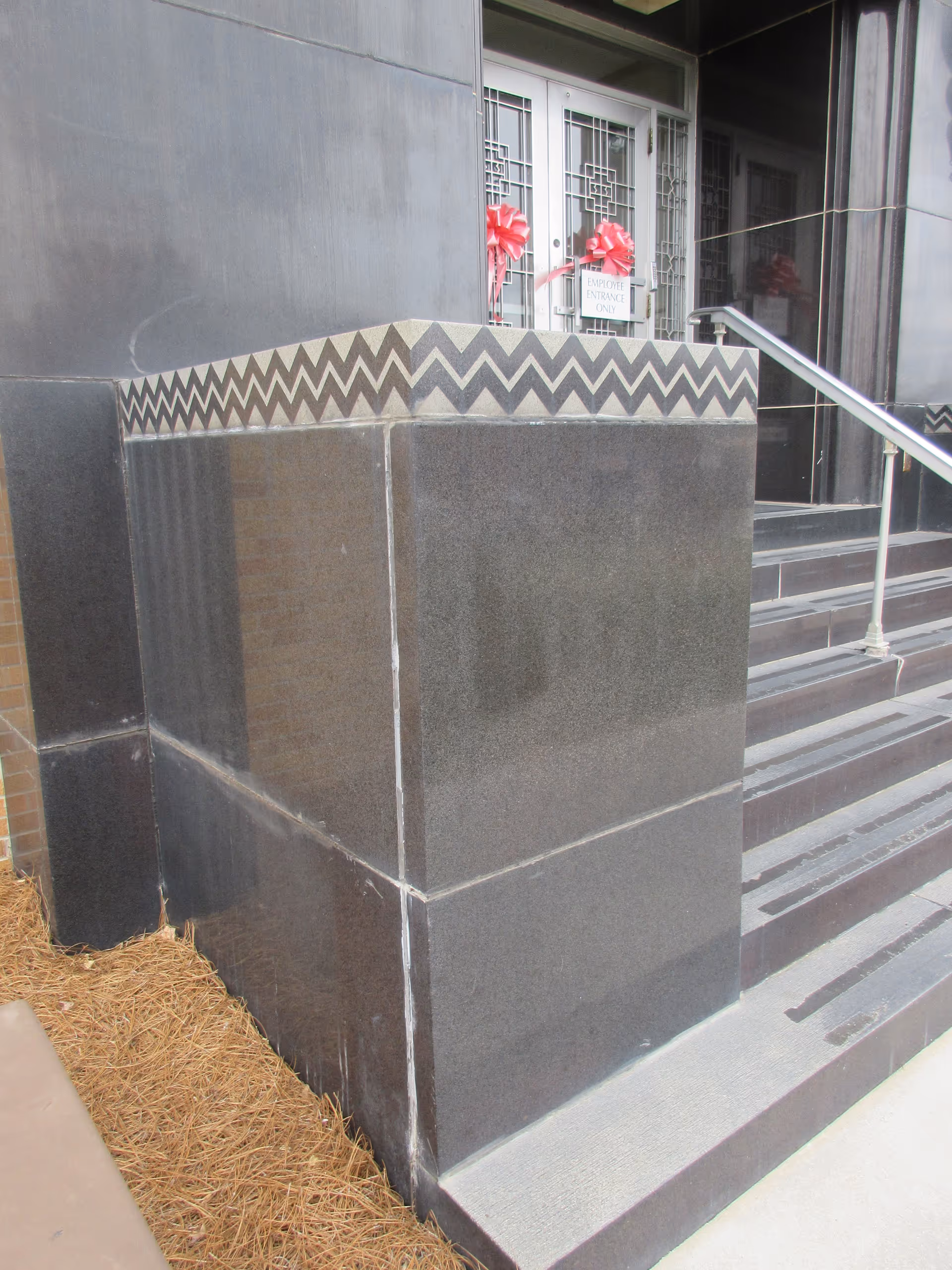 Front entrance of a dark stone building with stairs, railing, and pink ribbon decorations.