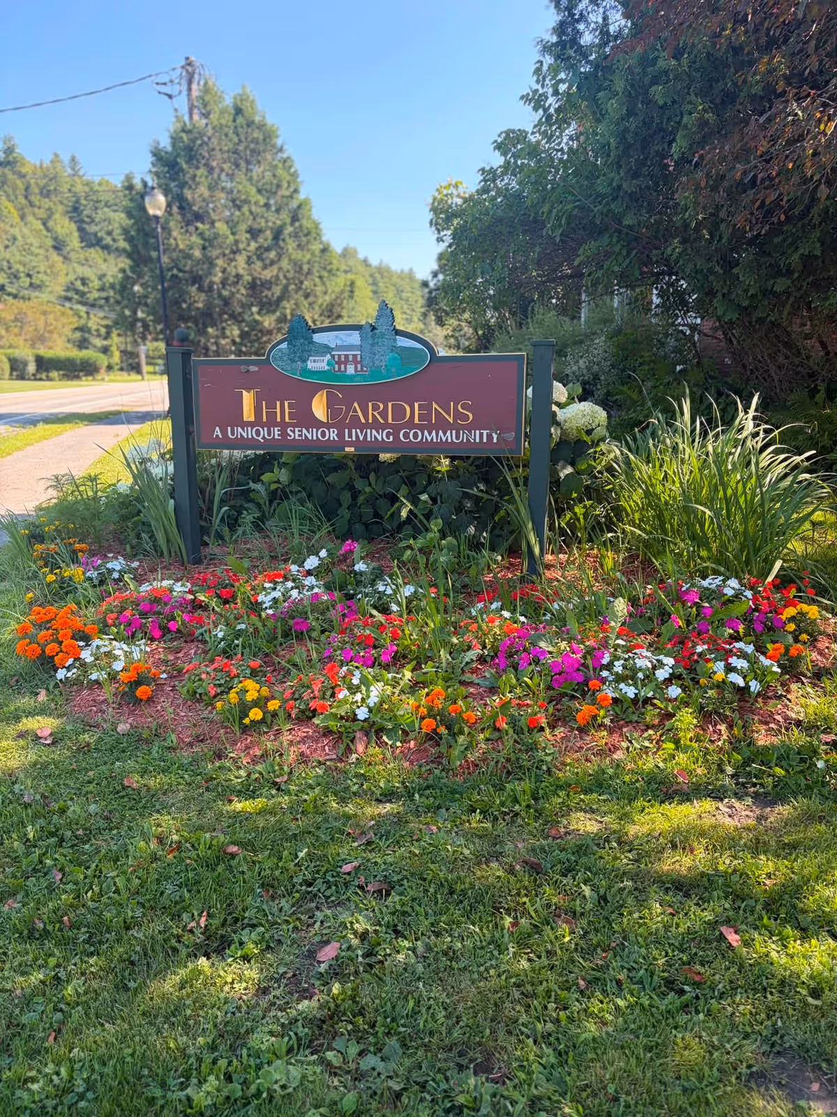 Colorful flower bed surrounds a sign reading The Gardens: A unique senior living community.