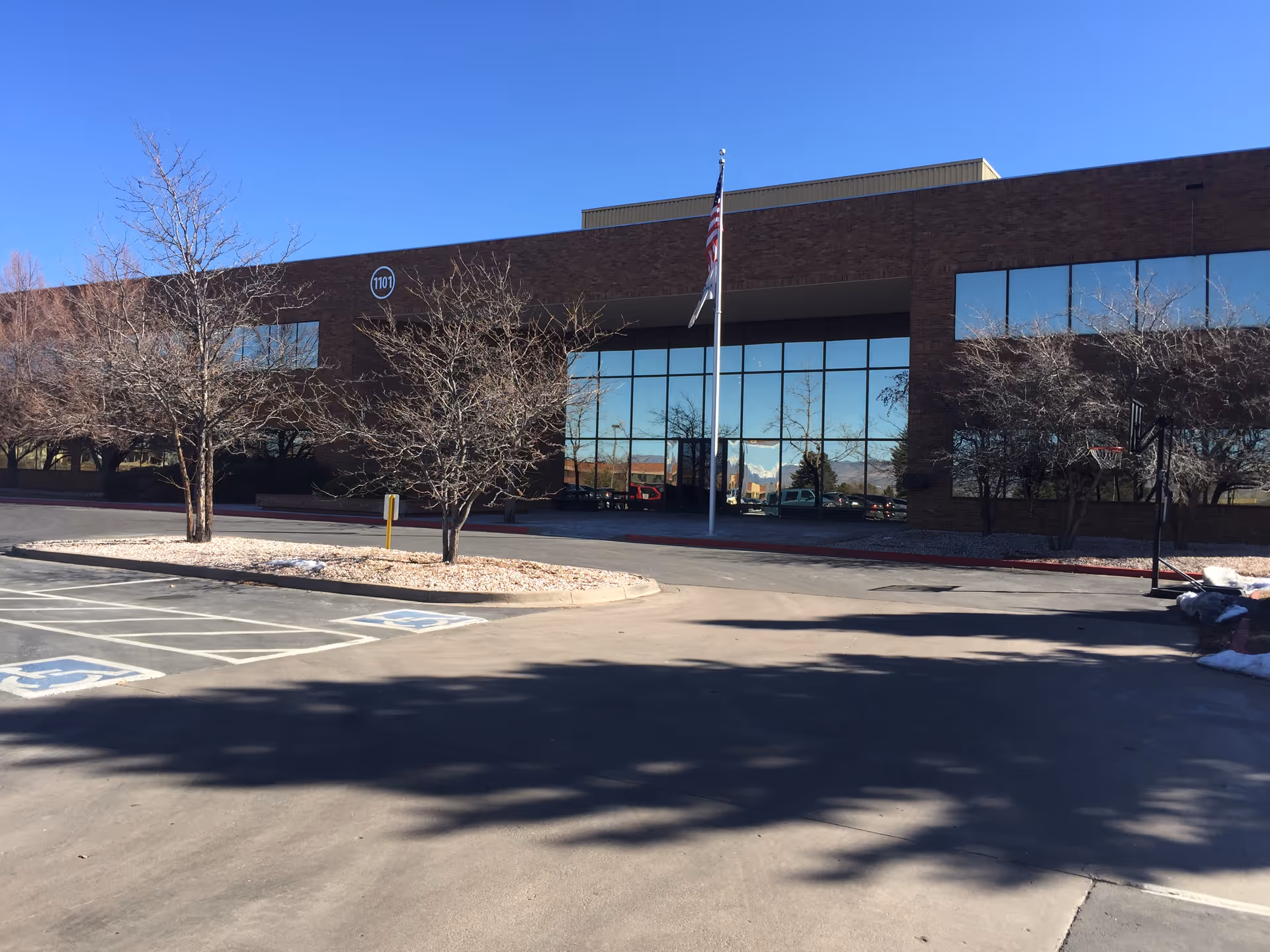 Brick building front with glass entrance, flagpole, and surrounding parking.