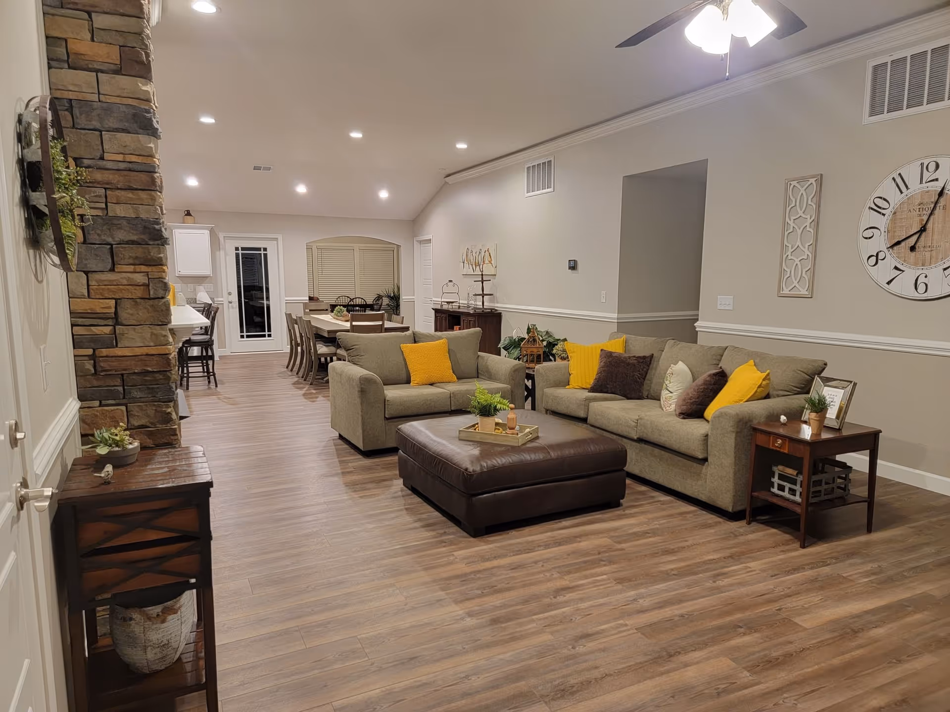 Spacious living room with beige sofas, yellow cushions, and an ottoman in a warm, open layout.