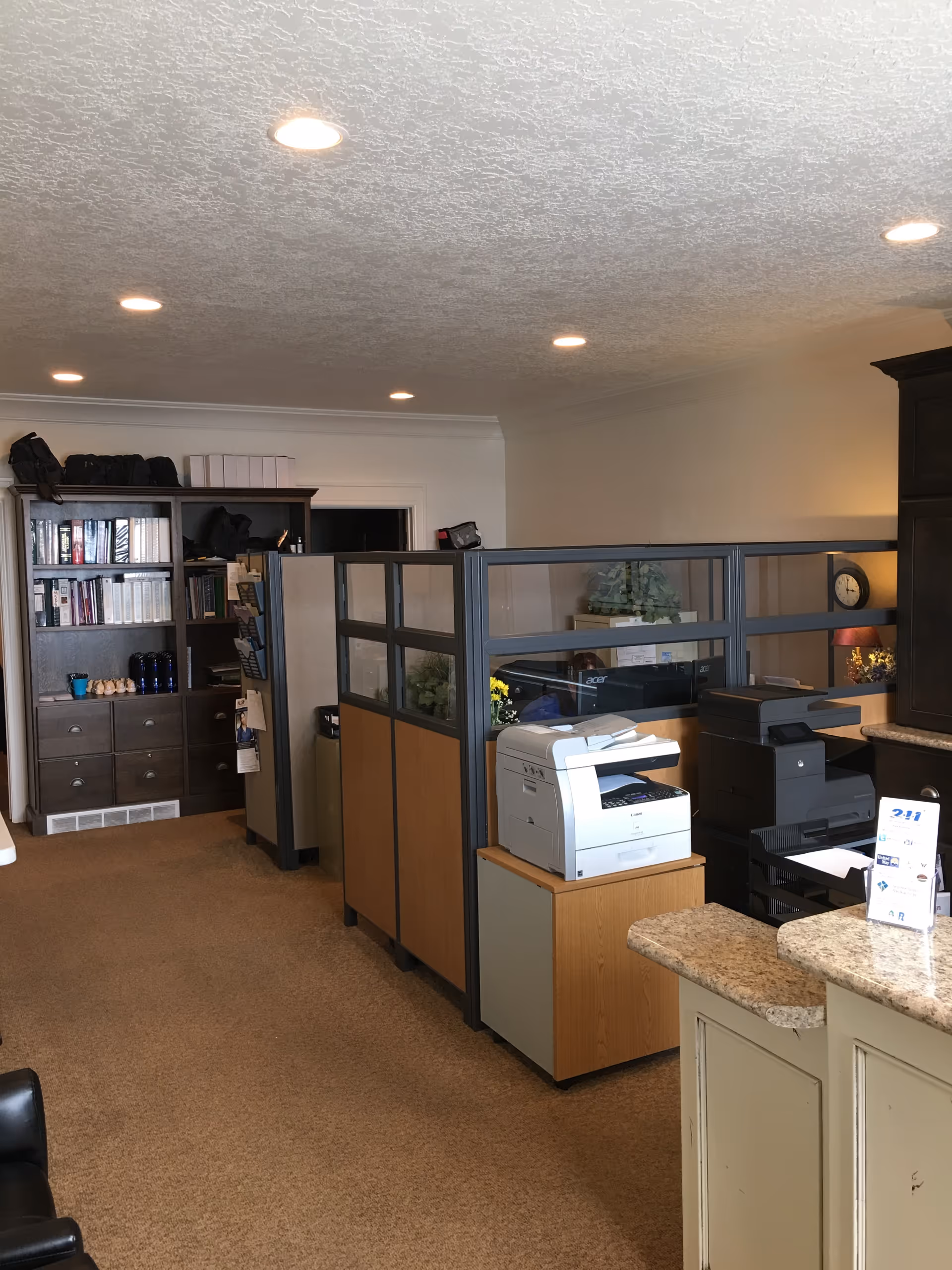 Interior office area with cubicles, a printer, and a bookshelf in a senior facility.