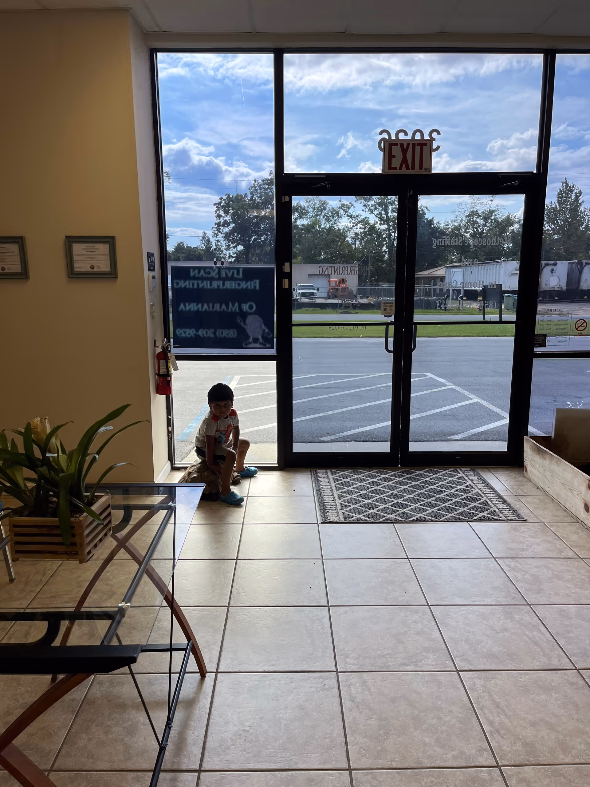 A child sits on a tiled lobby floor beside glass exit doors.