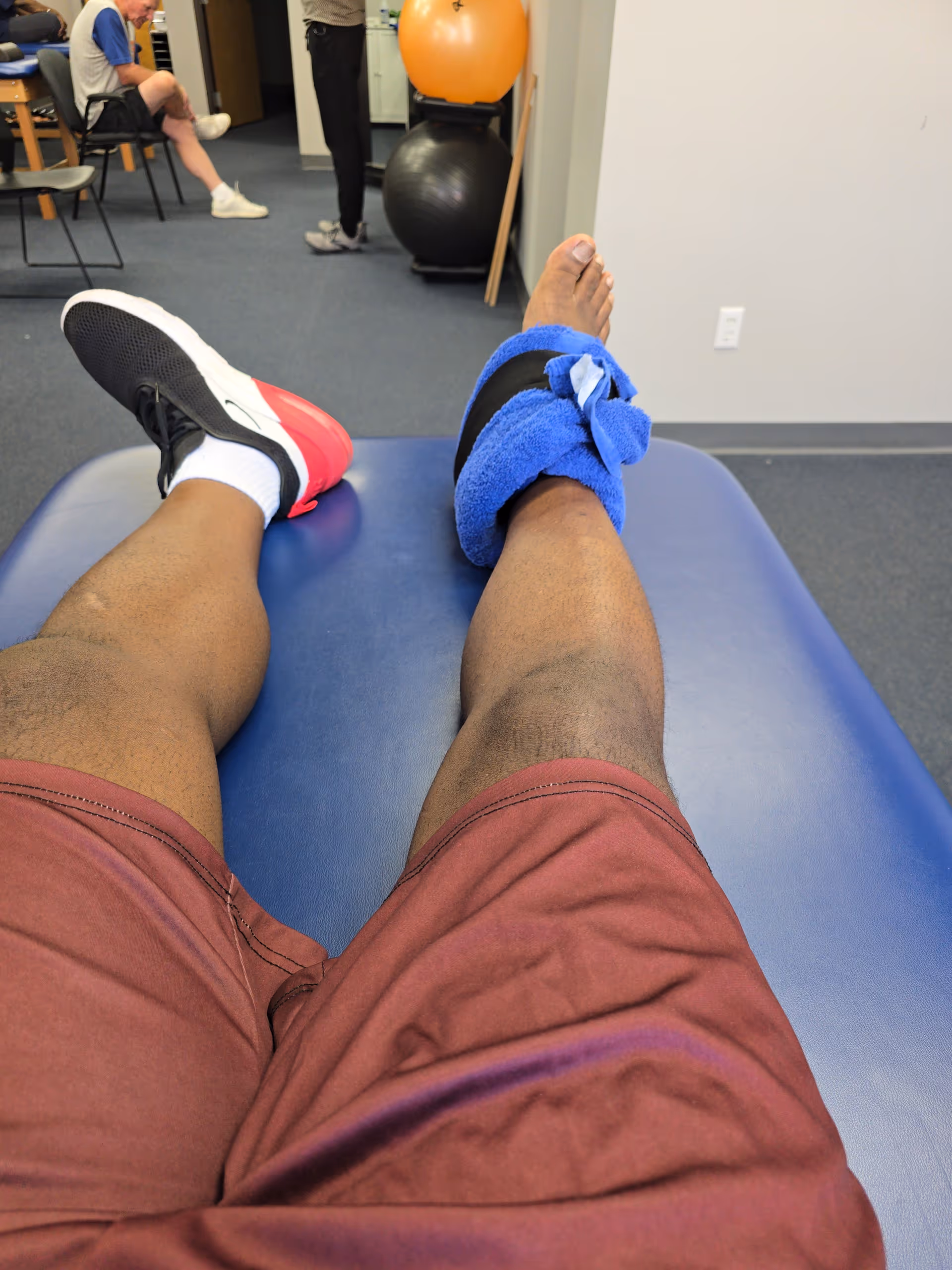 View of legs on a blue therapy table; ankle wrapped; exercise room with equipment.