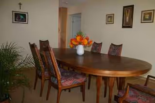 A dining room with an oval wooden table, chairs, a flower vase, and wall decor.