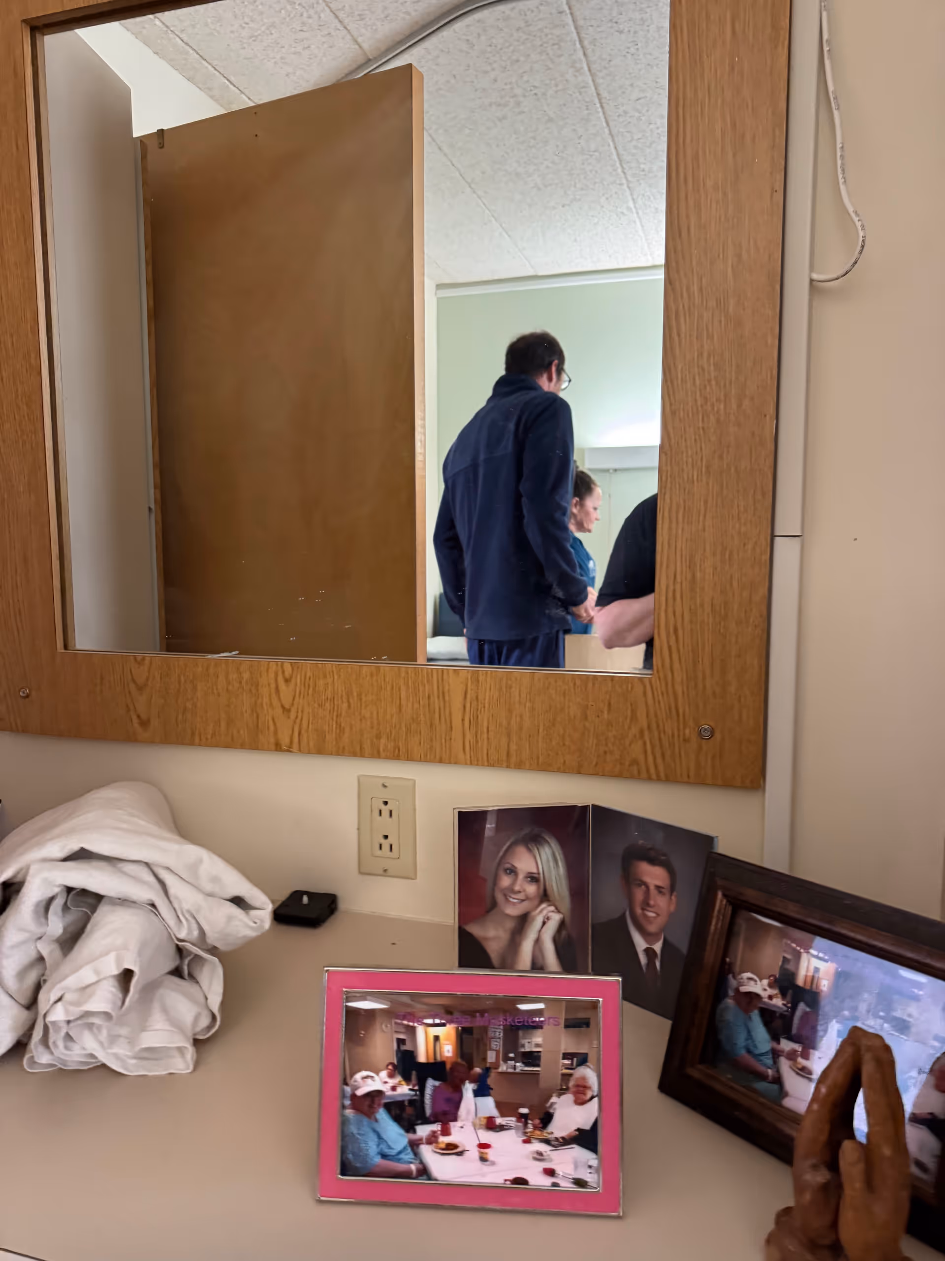Wood-framed mirror above a cluttered counter with photos and people reflected.
