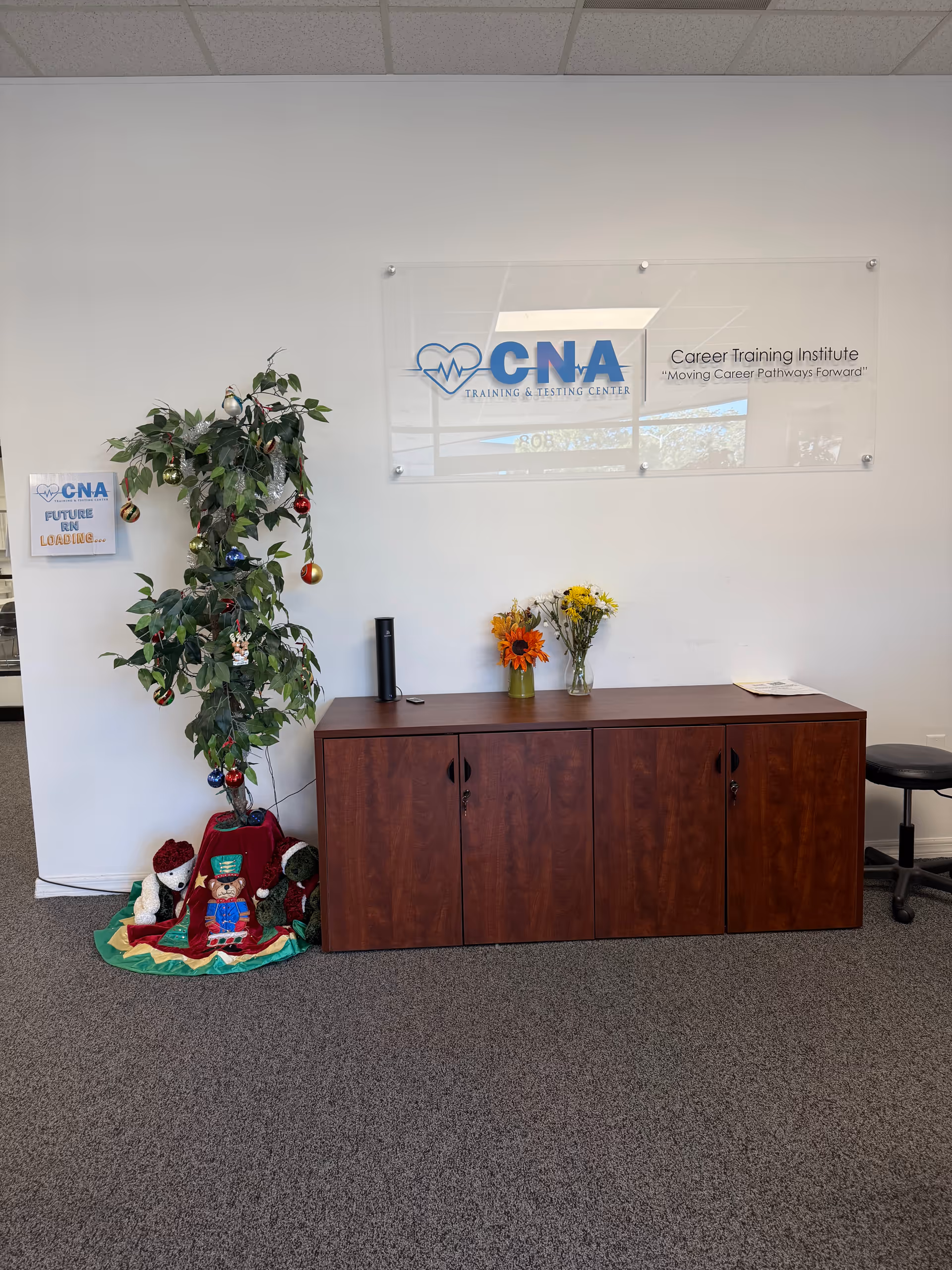 Interior reception area with wood cabinet, decorated Christmas tree, flowers, and CNA sign on wall.
