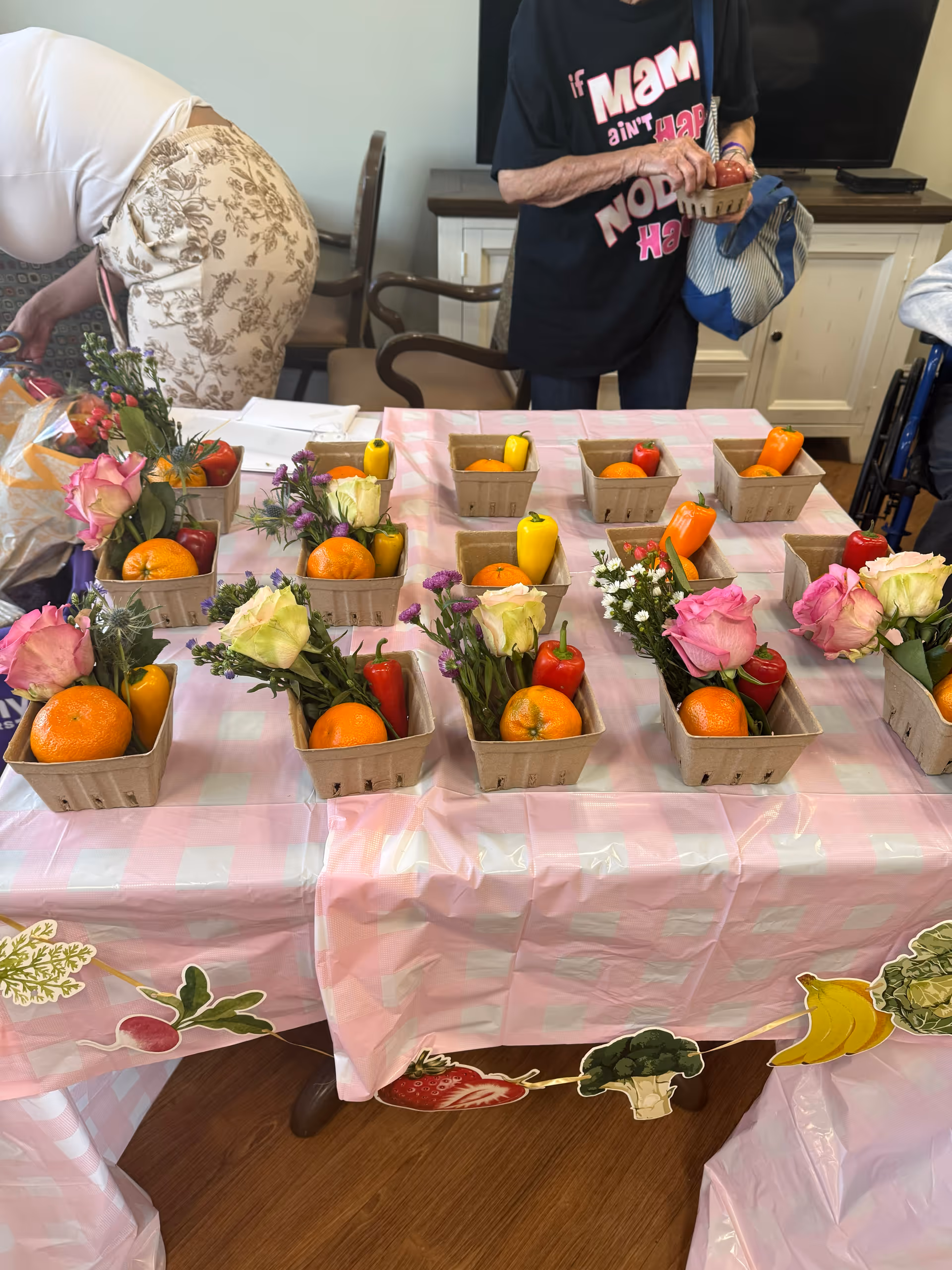 Table with fruit baskets and flowers on a pink checkered table in an indoor common area.
