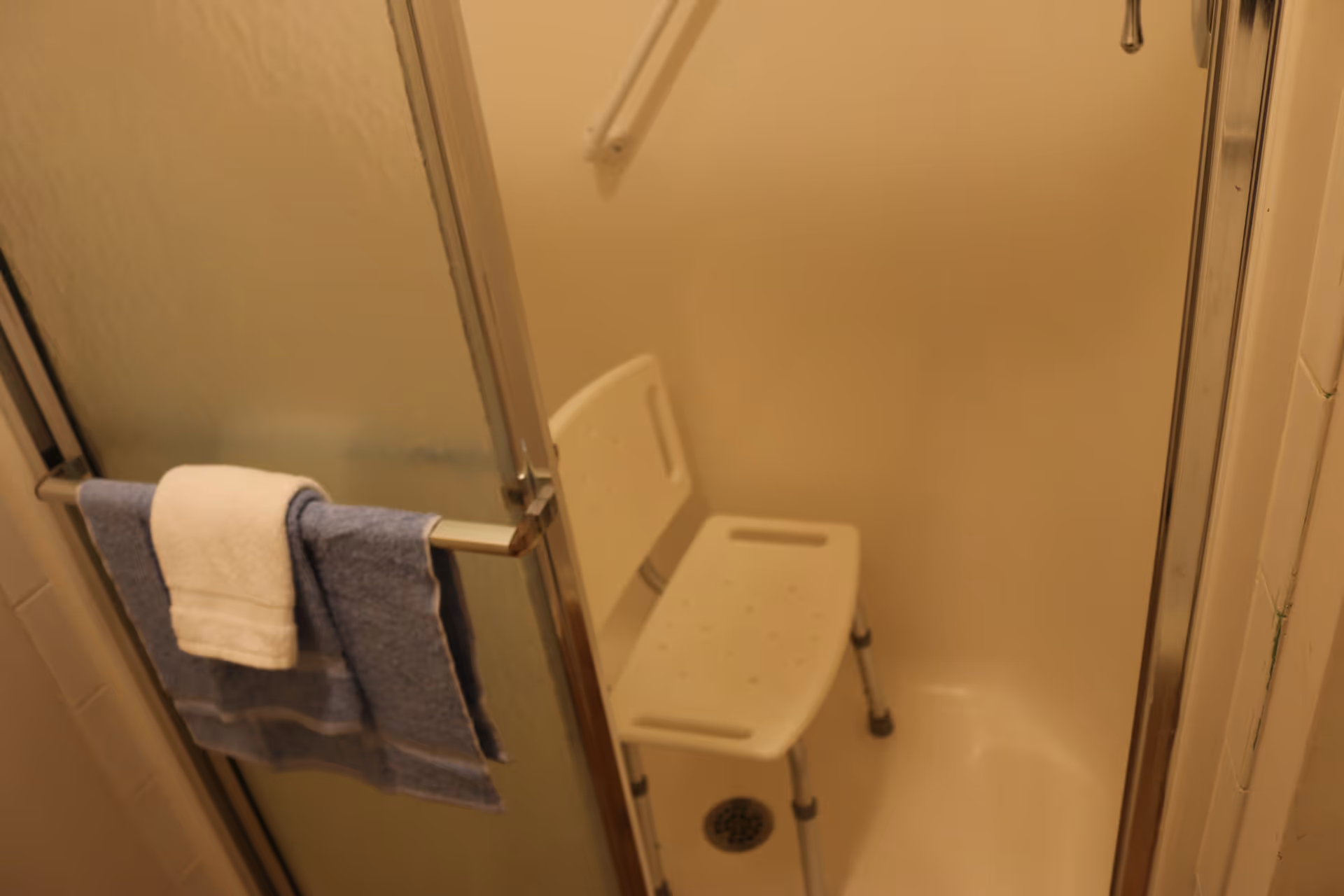 Shower stall with sliding glass doors and a foldable shower chair in a bathroom.