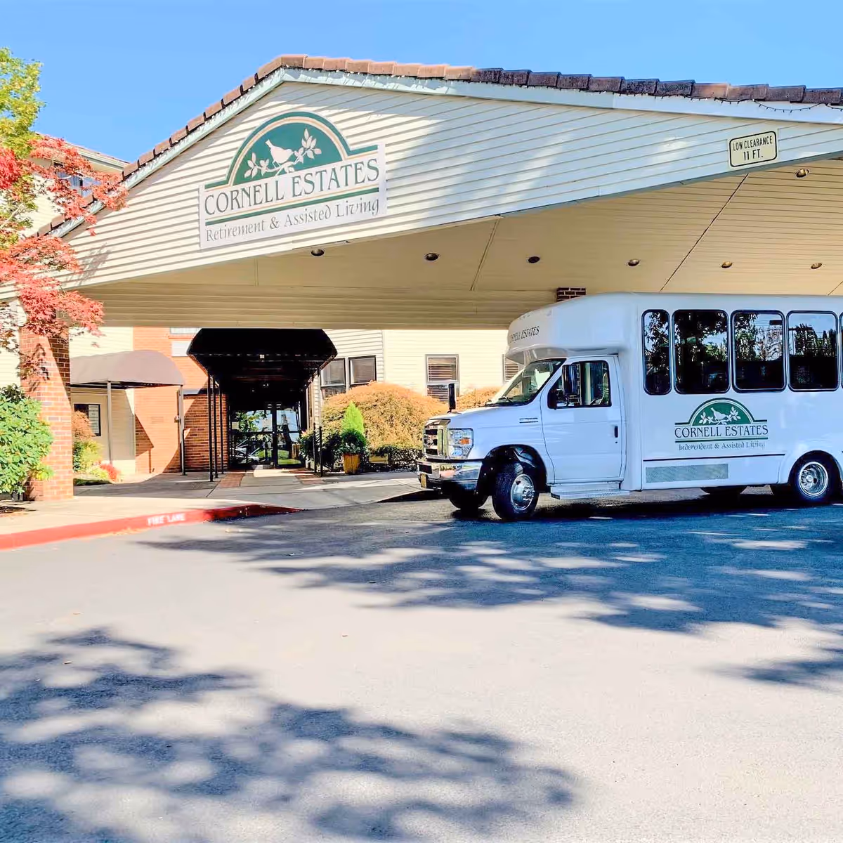 White Cornell Estates building front with driveway, entrance canopy, and a parked service bus.