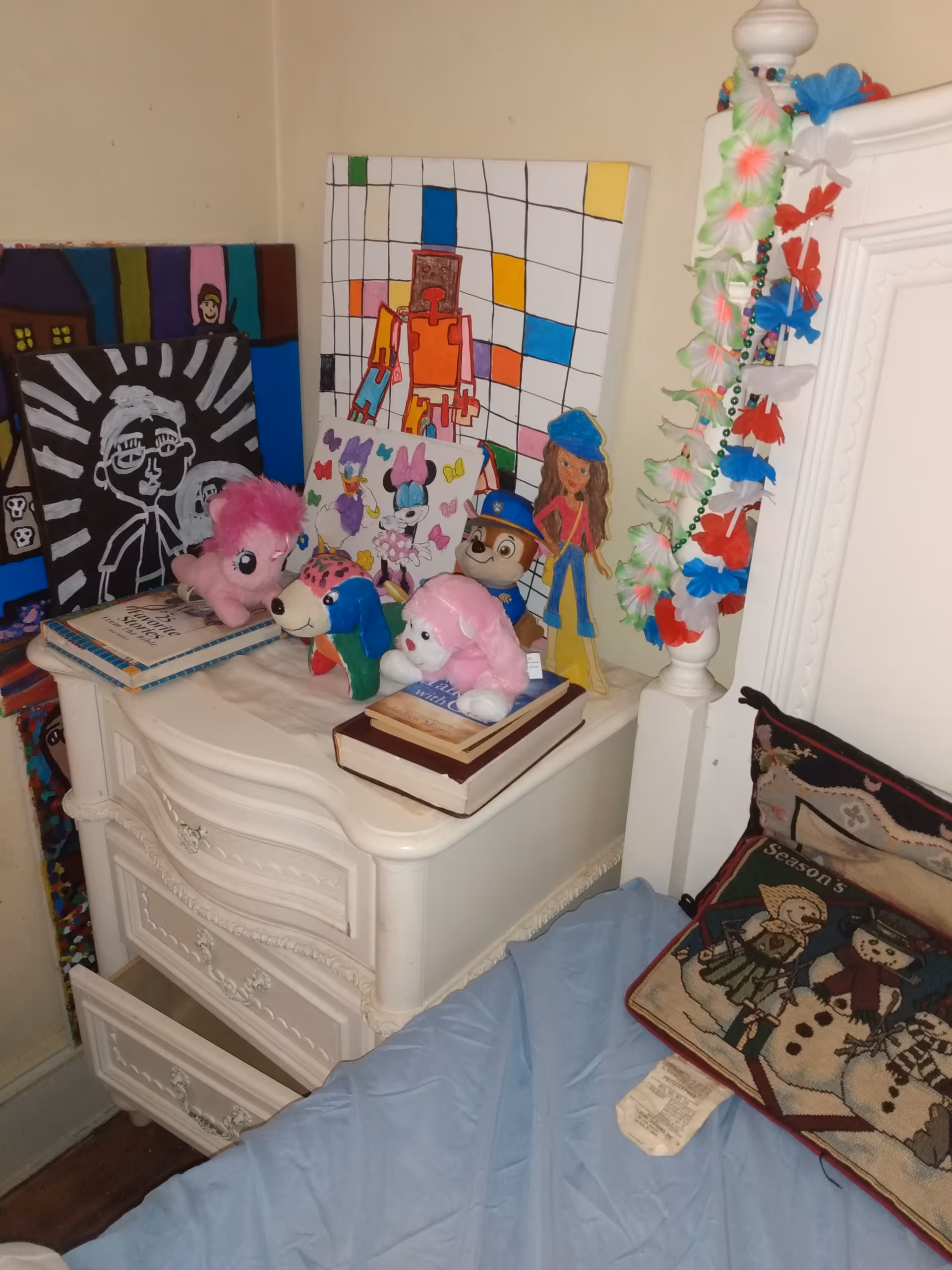 White dresser cluttered with stuffed animals, books, and colorful children's drawings.