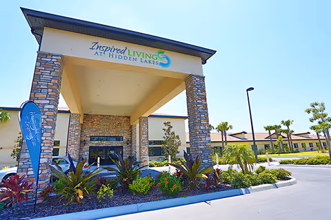 Front entrance of Inspired Living at Hidden Lakes with stone pillars and landscaped grounds.