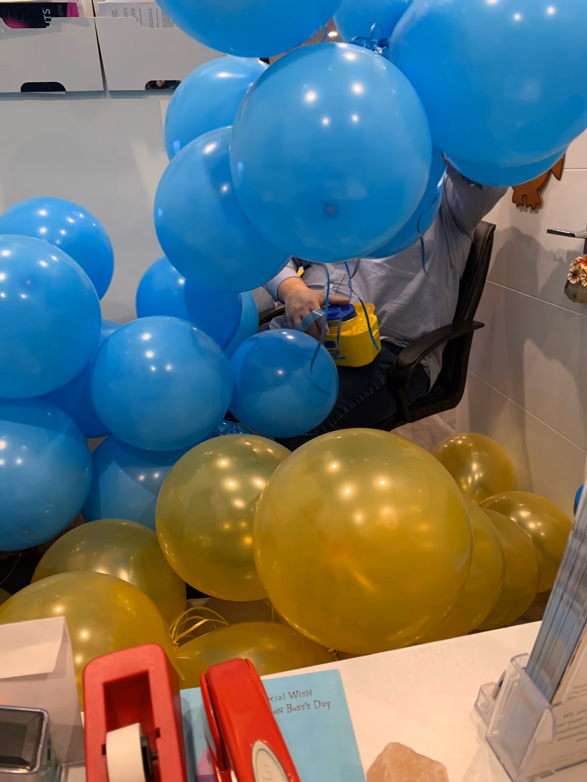 Indoor office area with blue and gold balloons around a desk.