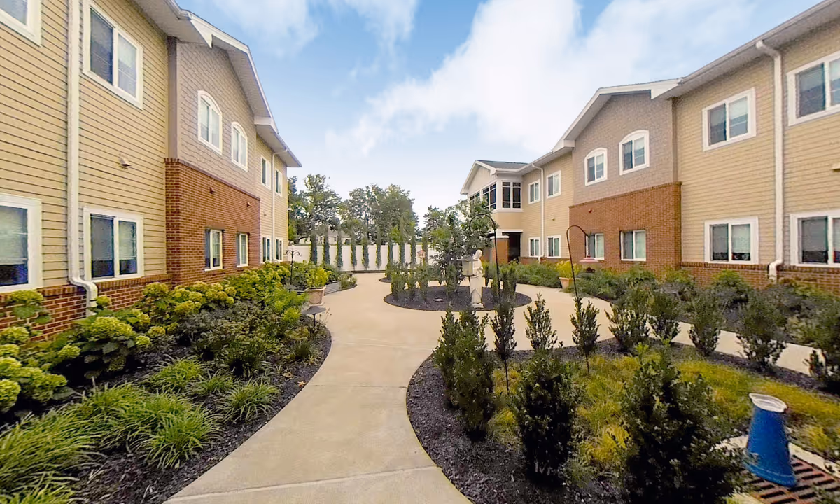 Two beige apartment-style buildings enclose a landscaped courtyard with a curved concrete walkway.