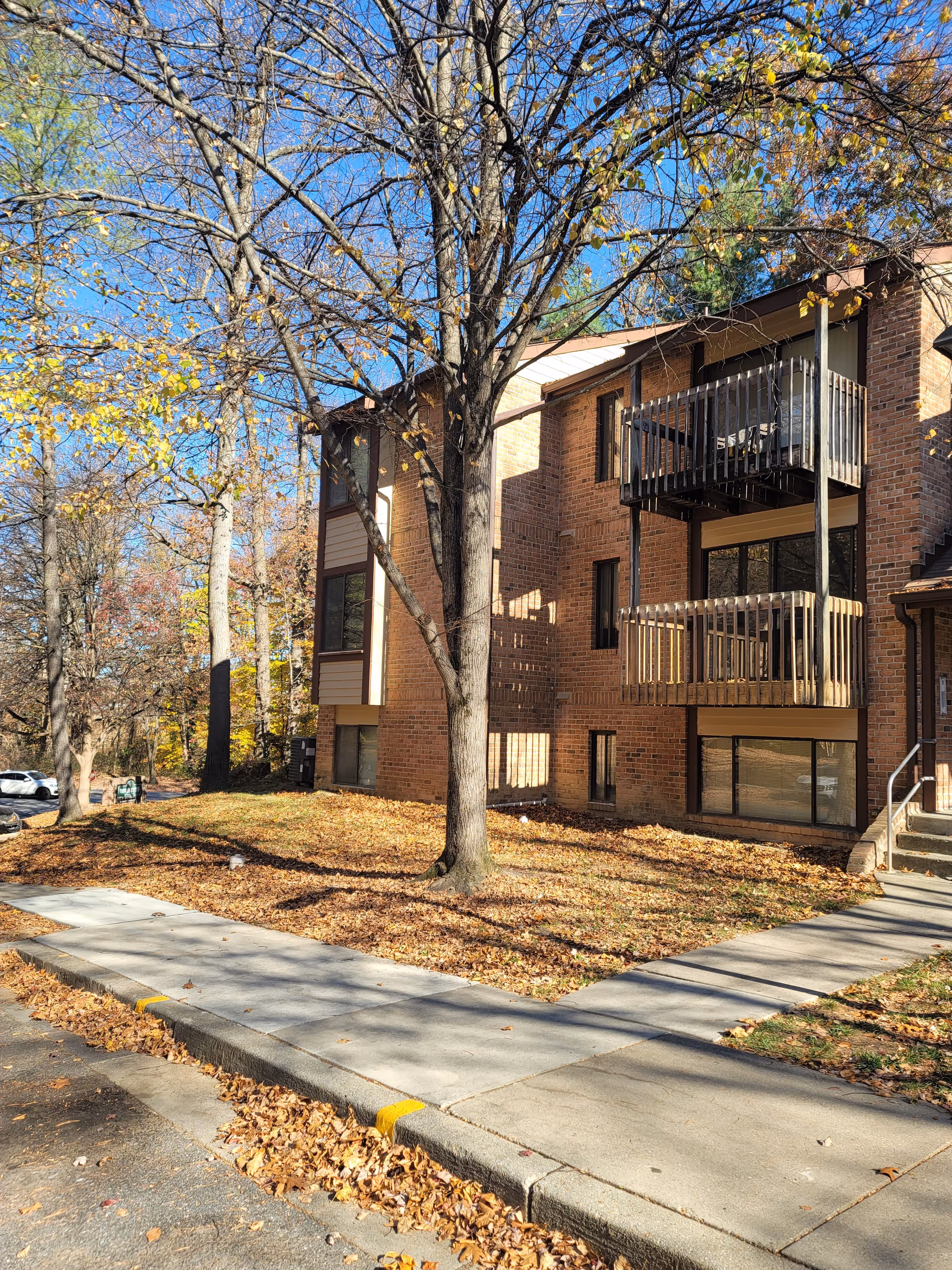 Exterior view of a brick senior living building with balconies amid autumn trees.