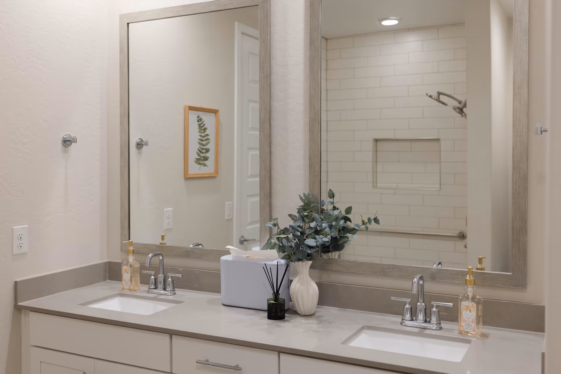 Two-sink bathroom vanity with large mirrors and a shower visible in the background.