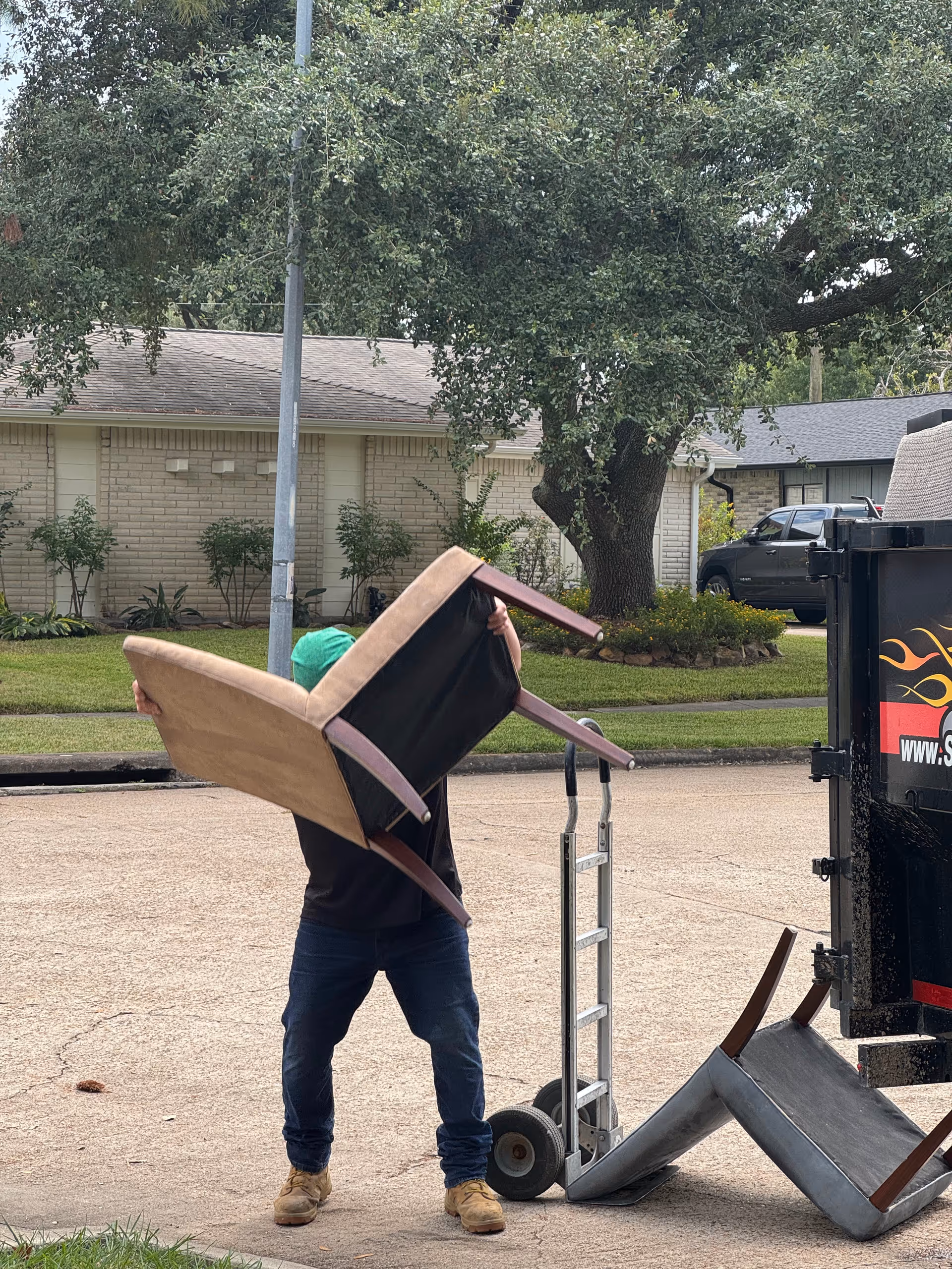Person moves a sofa toward a dumpster in an outdoor area beside a facility.