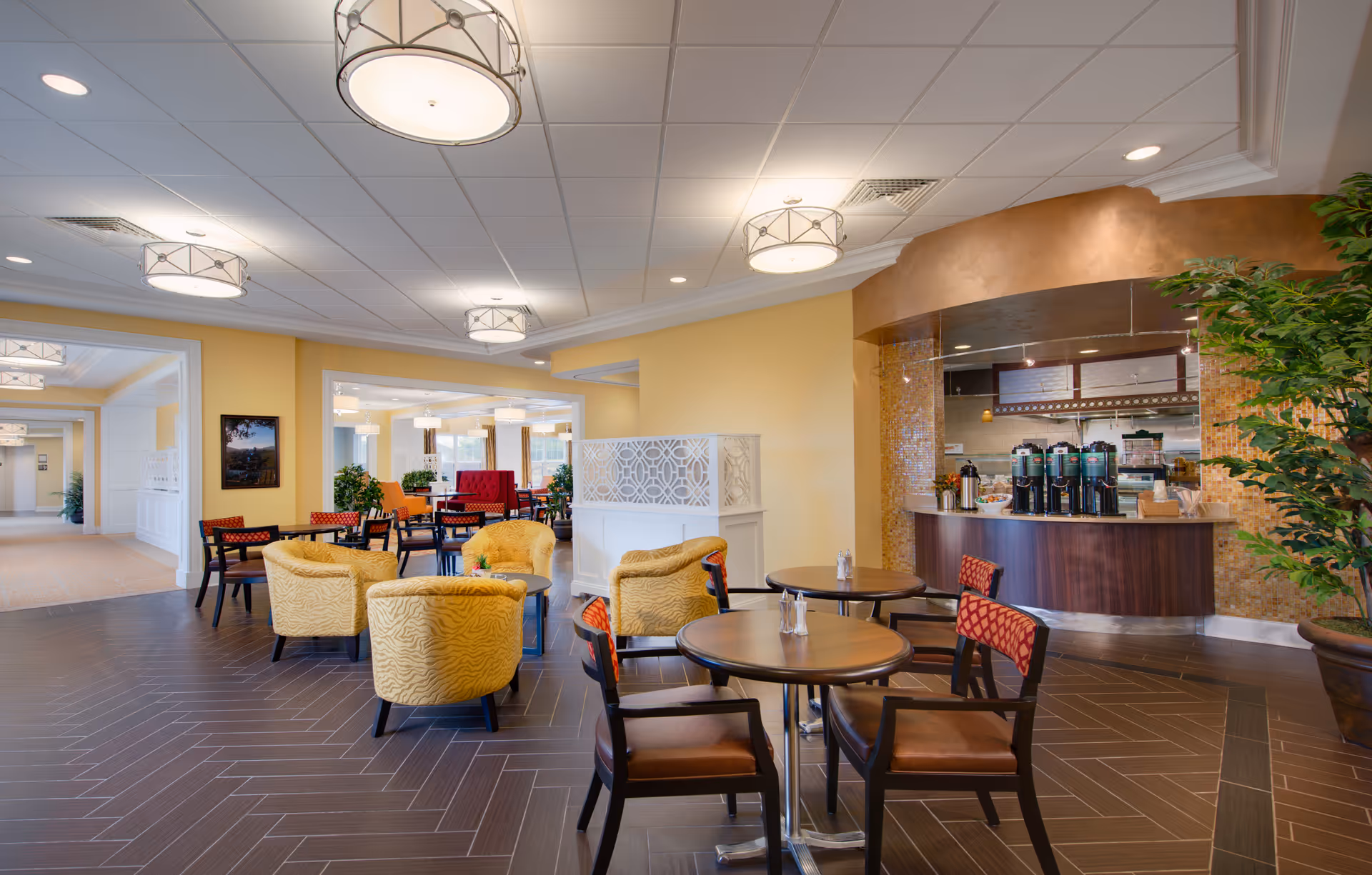 Spacious indoor lounge area with round tables, yellow chairs, and a beverage counter.