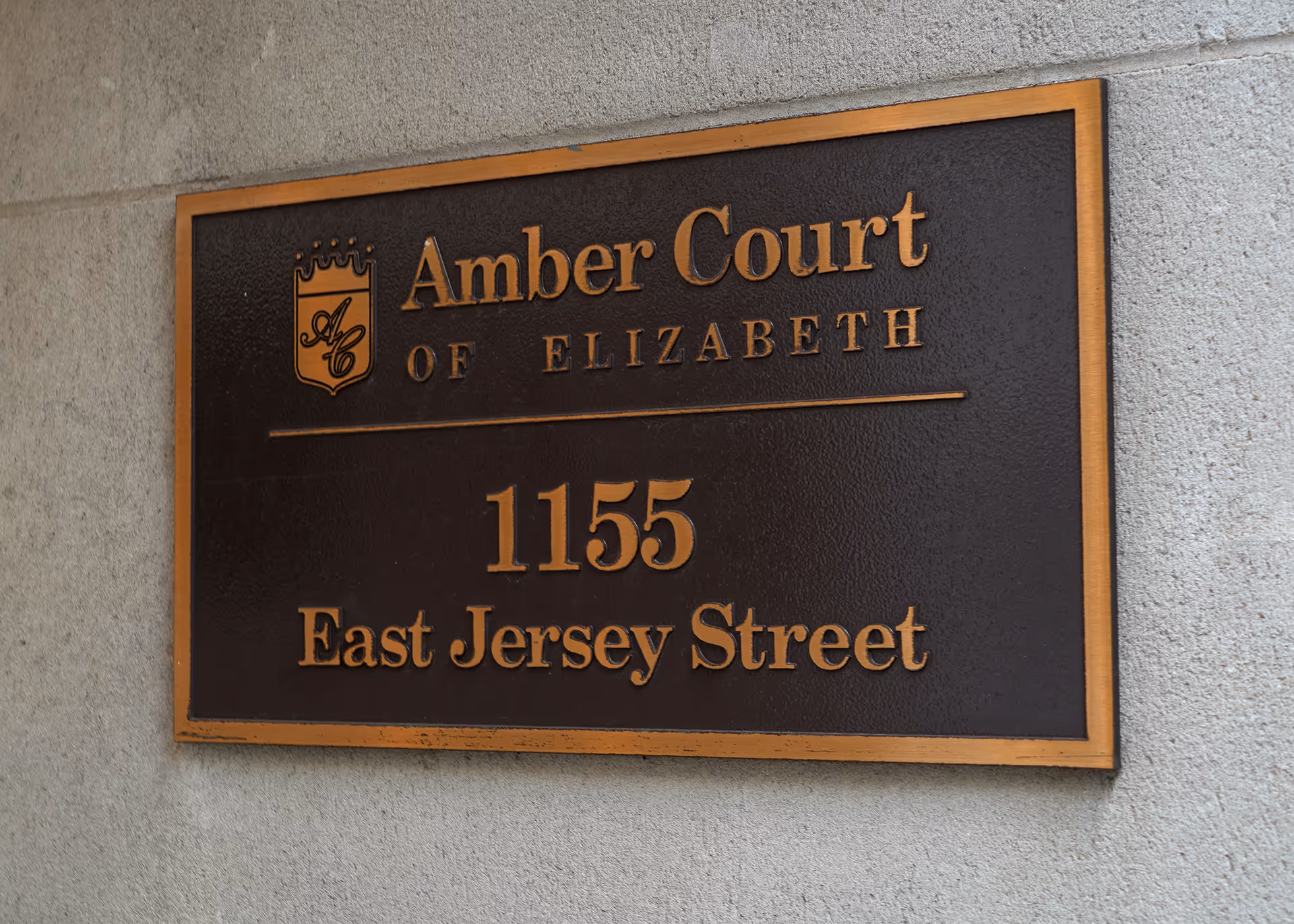 Bronze sign plaque on a concrete wall reads Amber Court of Elizabeth, 1155 East Jersey Street.