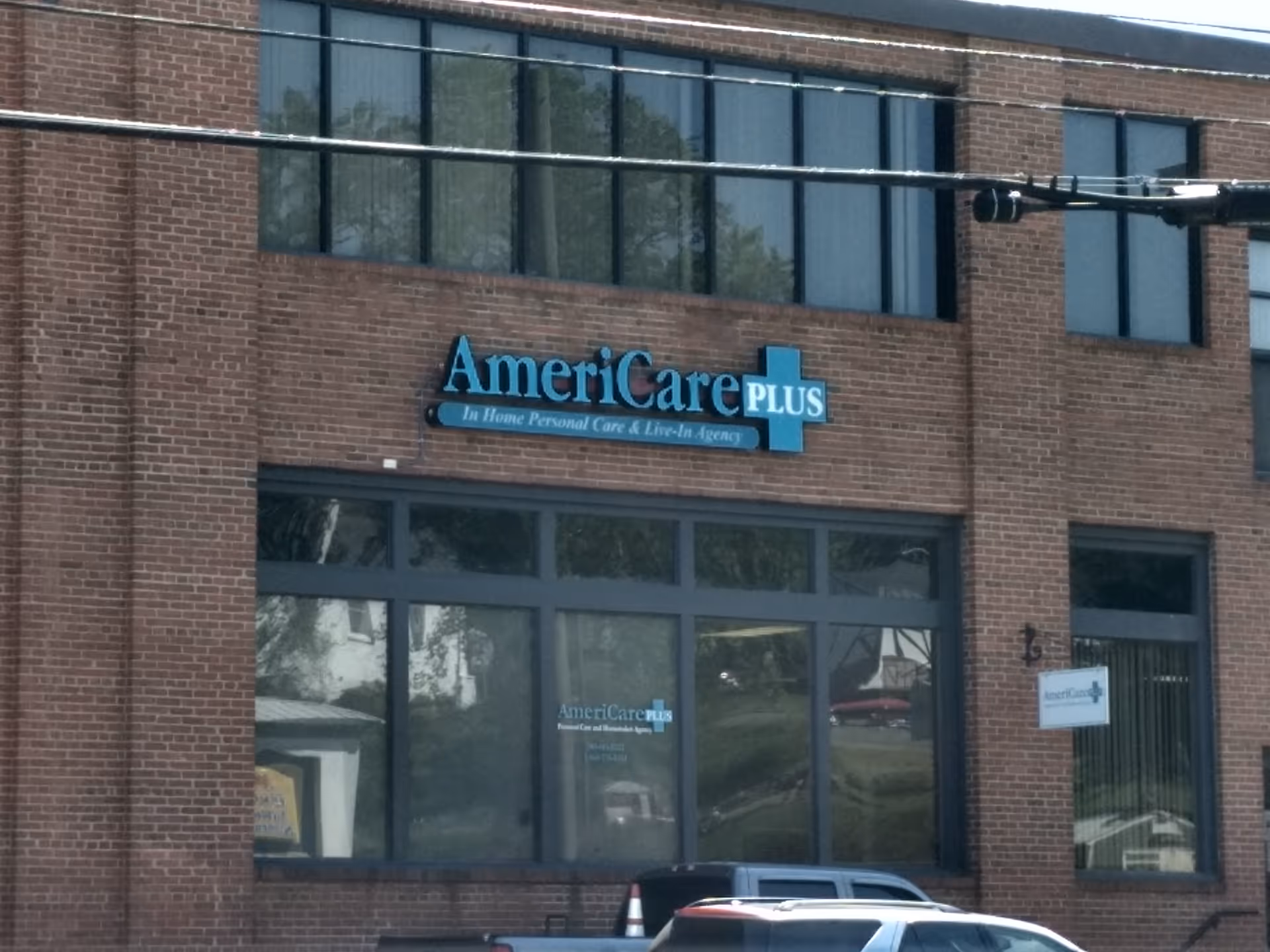 Brick building exterior featuring AmeriCare Plus sign and large glass storefront windows.