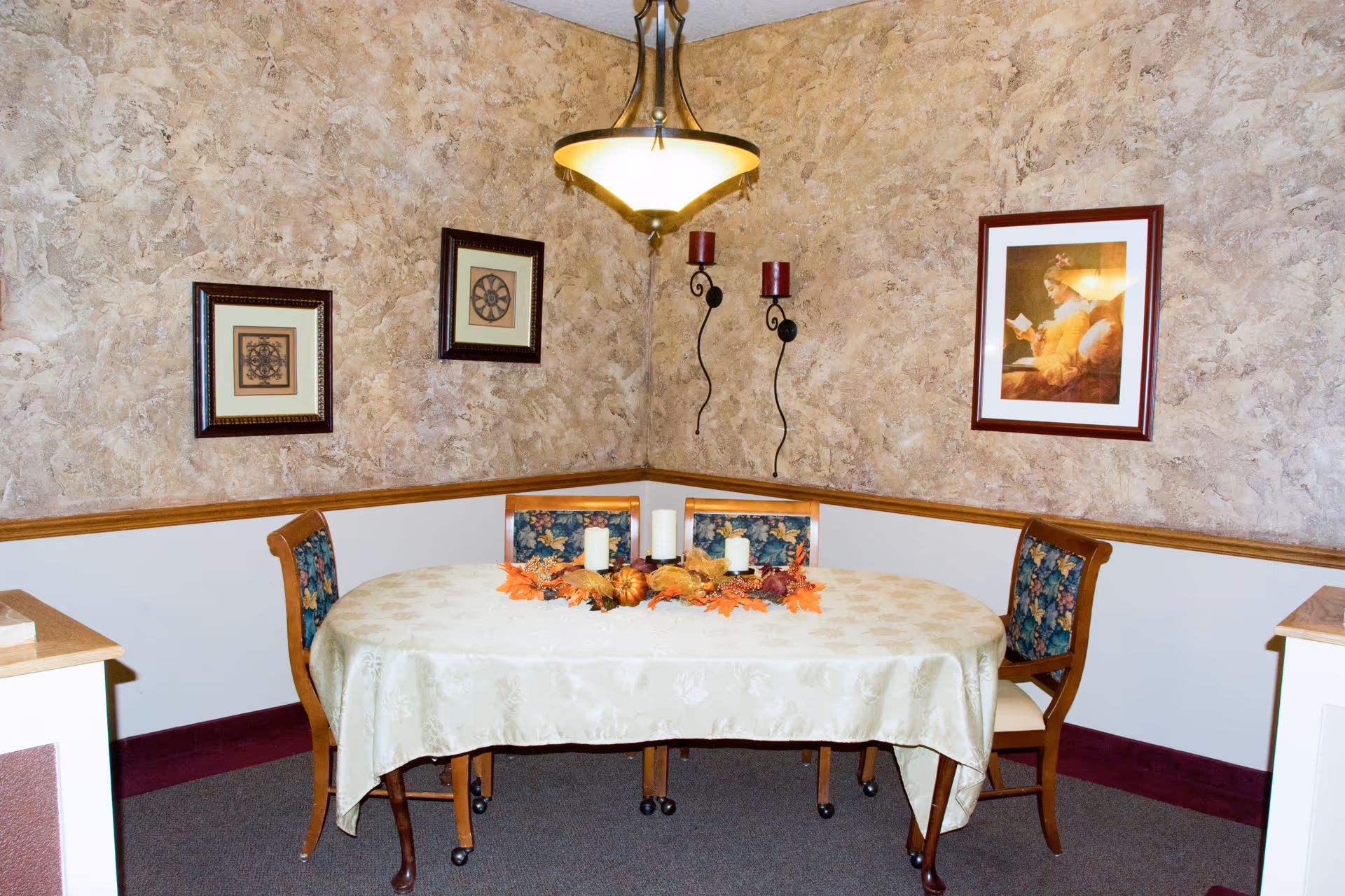 Corner dining nook with a round table, lit chandelier, and framed wall art.