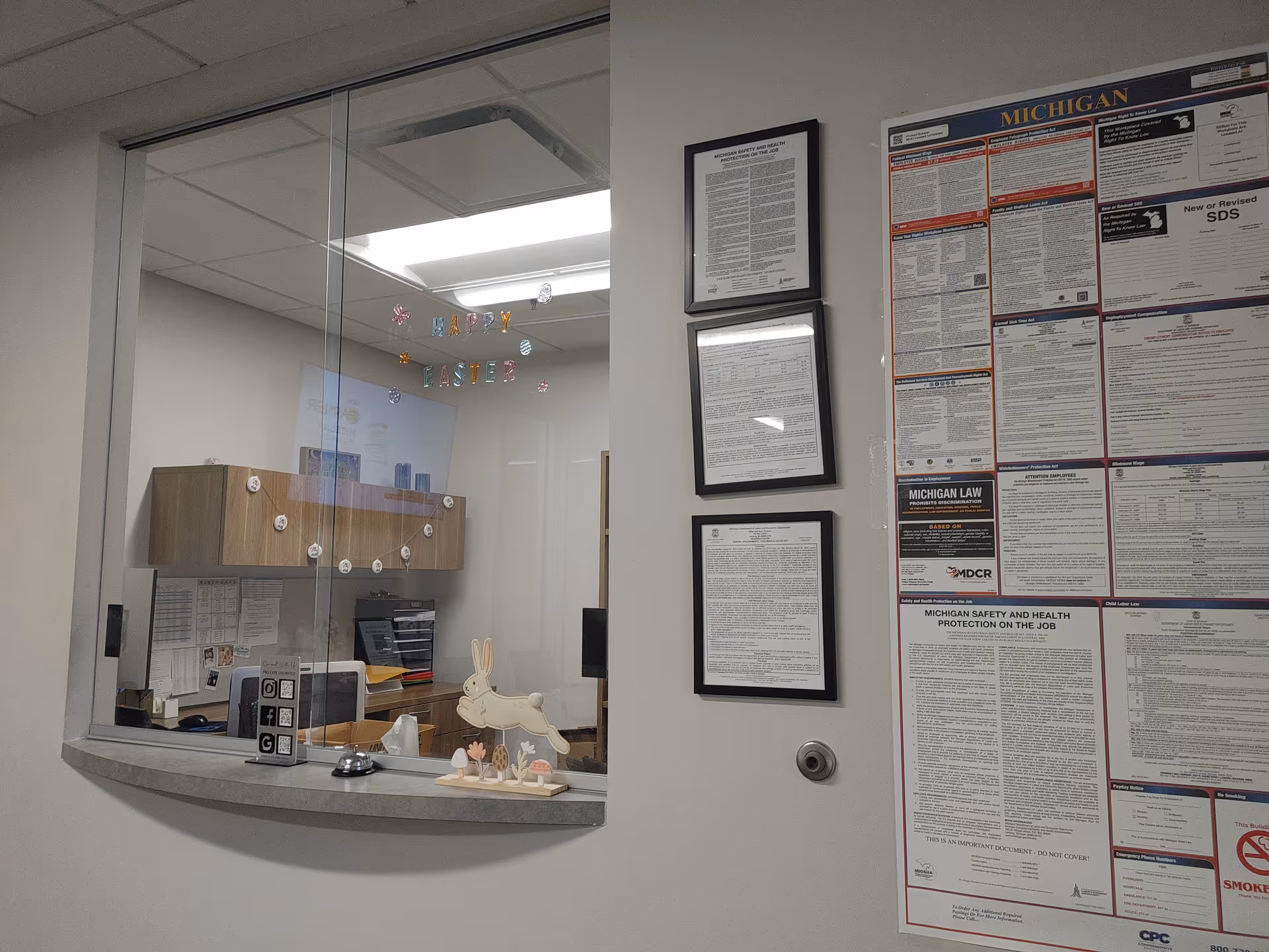 Inside a facility admin area, glass window reveals reception desk and framed posters.