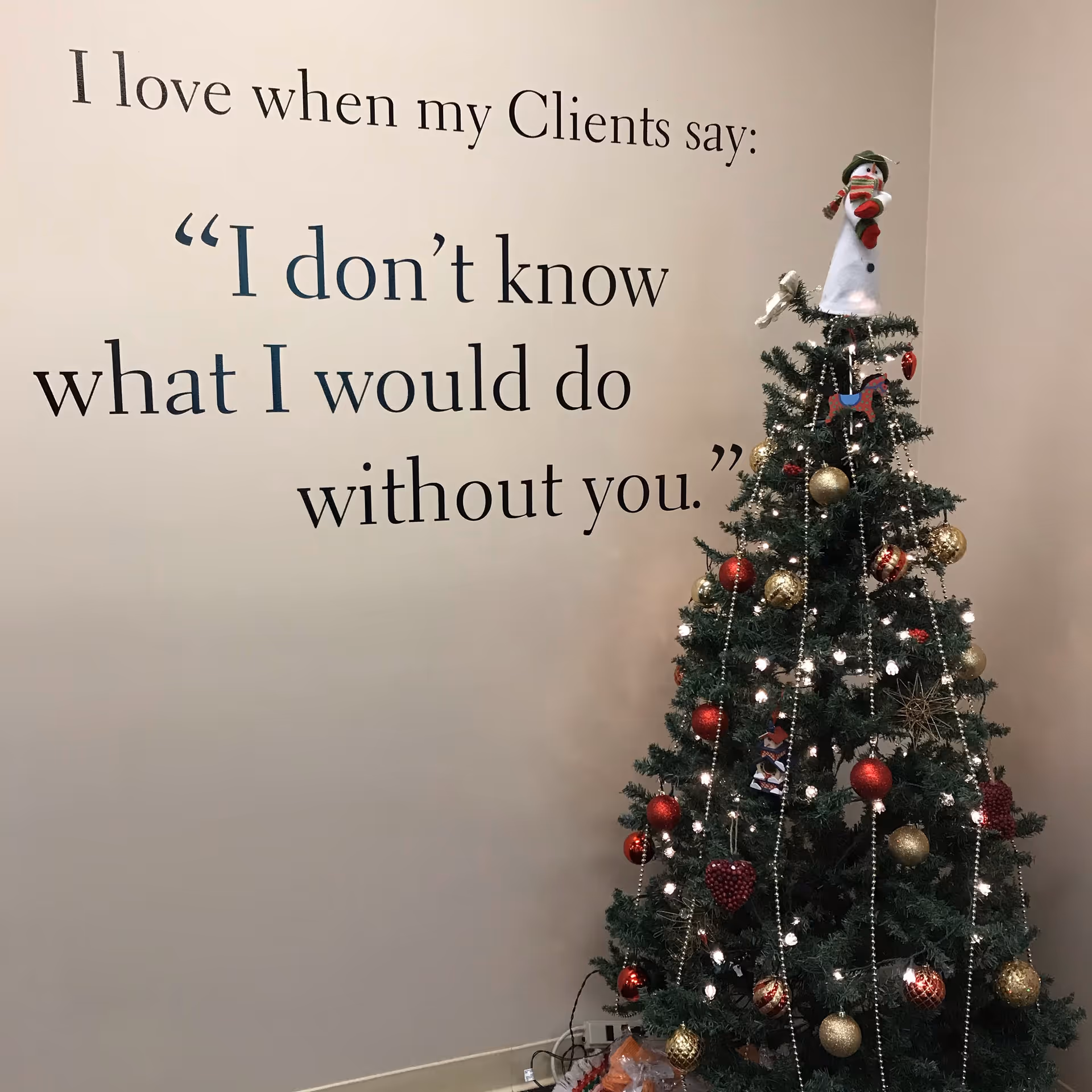 A decorated Christmas tree stands beside a wall with a quote in a hallway.