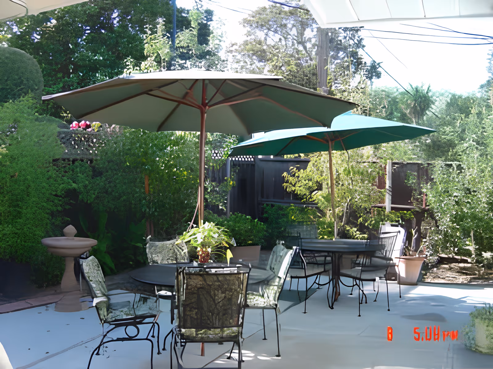 Outdoor seating area with tables, chairs, and umbrellas surrounded by greenery.