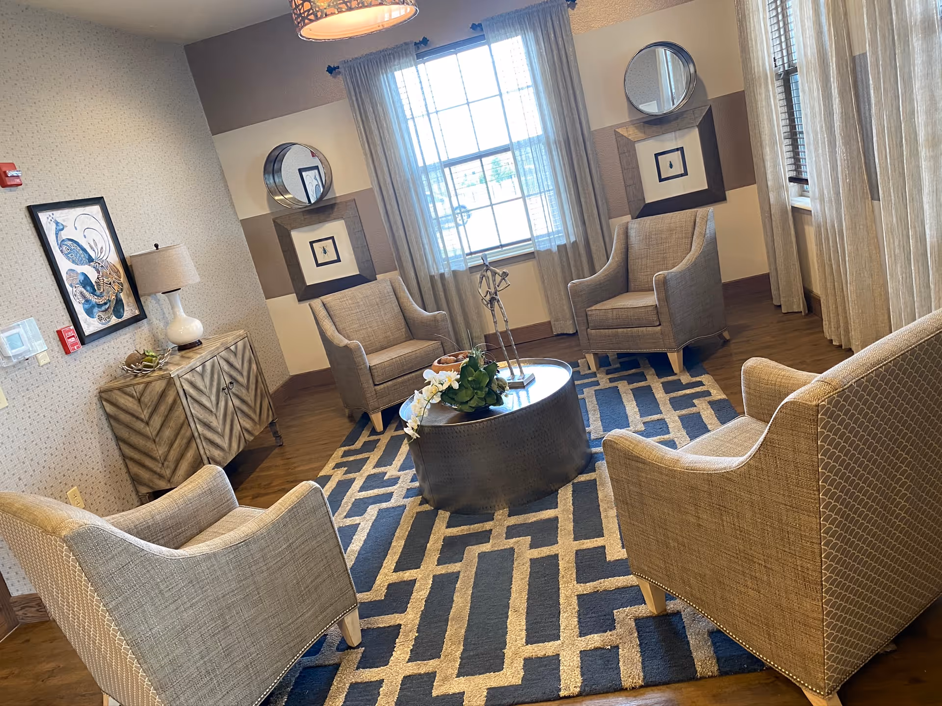 Cozy senior living lounge with beige upholstered chairs arranged around a round coffee table.