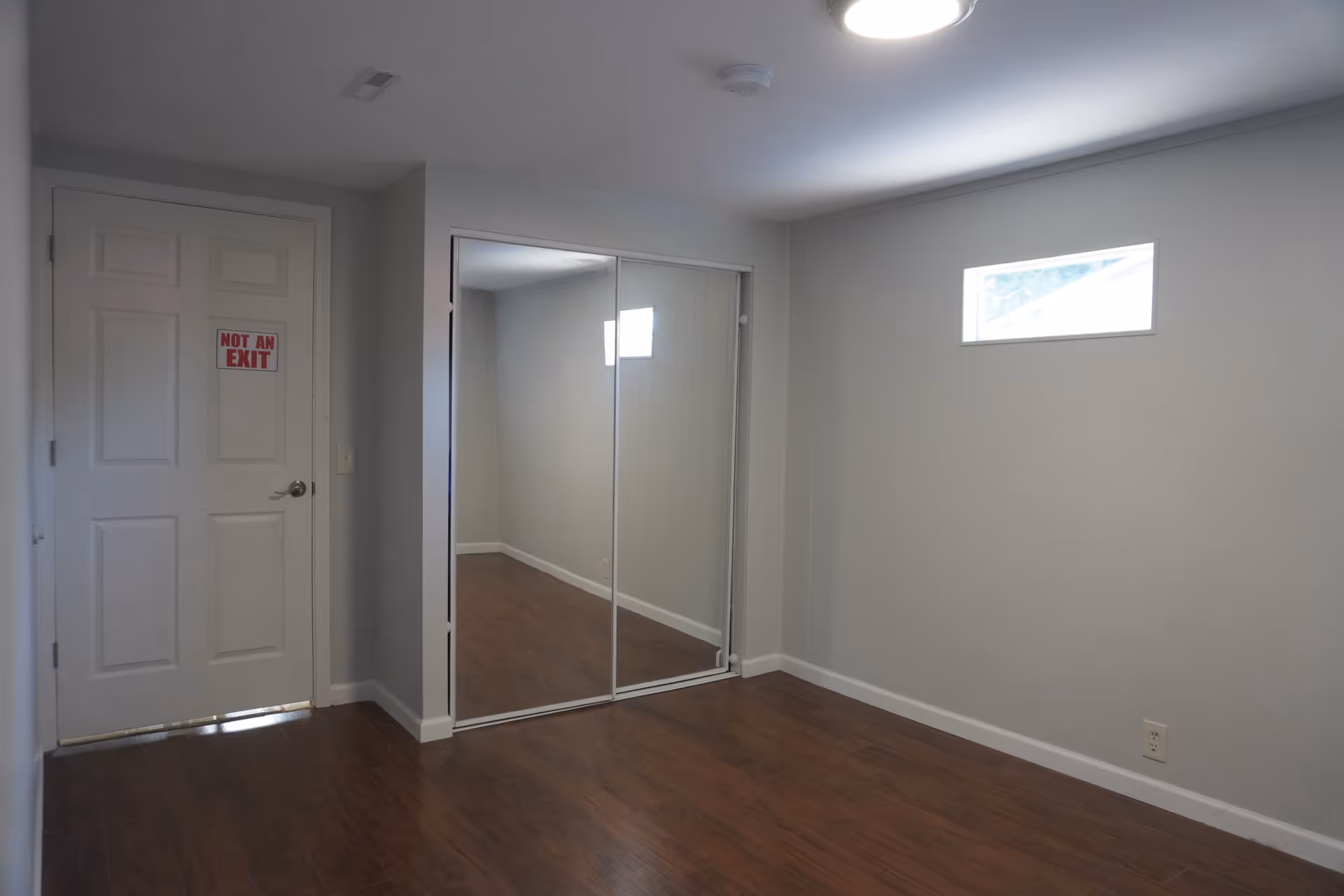 Small empty room with a mirrored closet door, window, and wood flooring.
