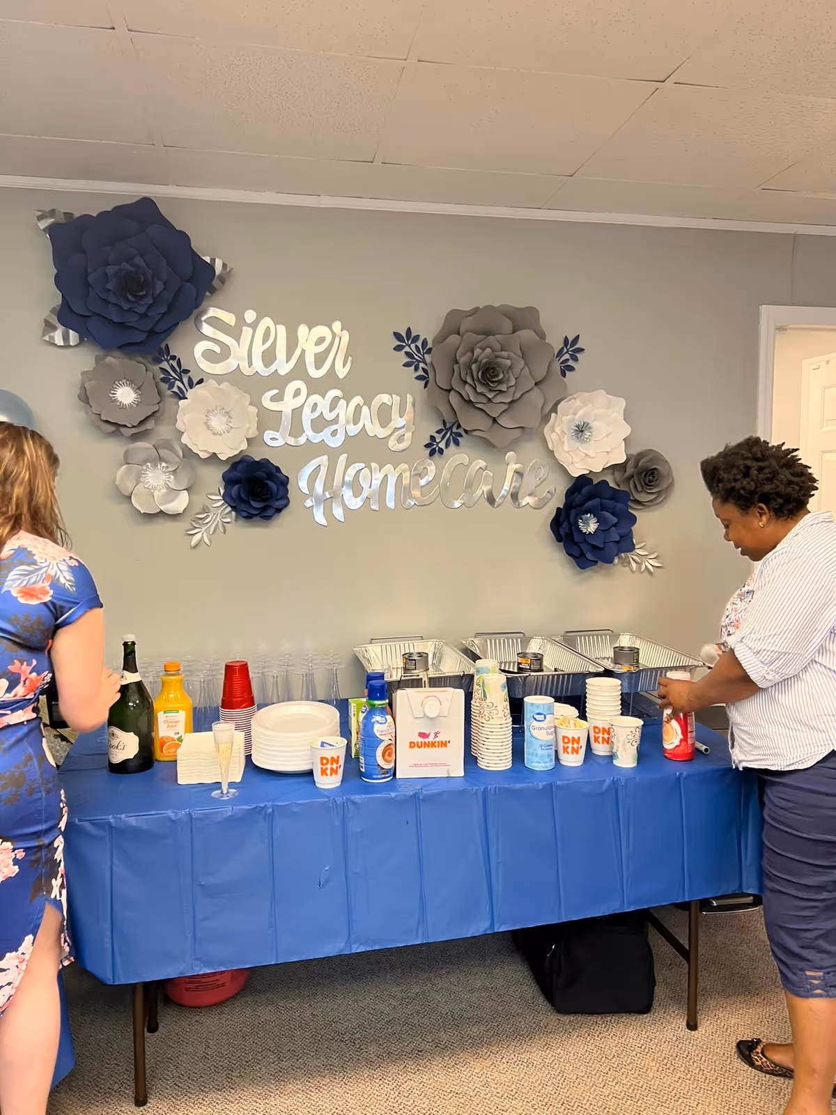 Indoor beverage station with blue tablecloth beneath a decorative Silver Legacy Home Care sign.