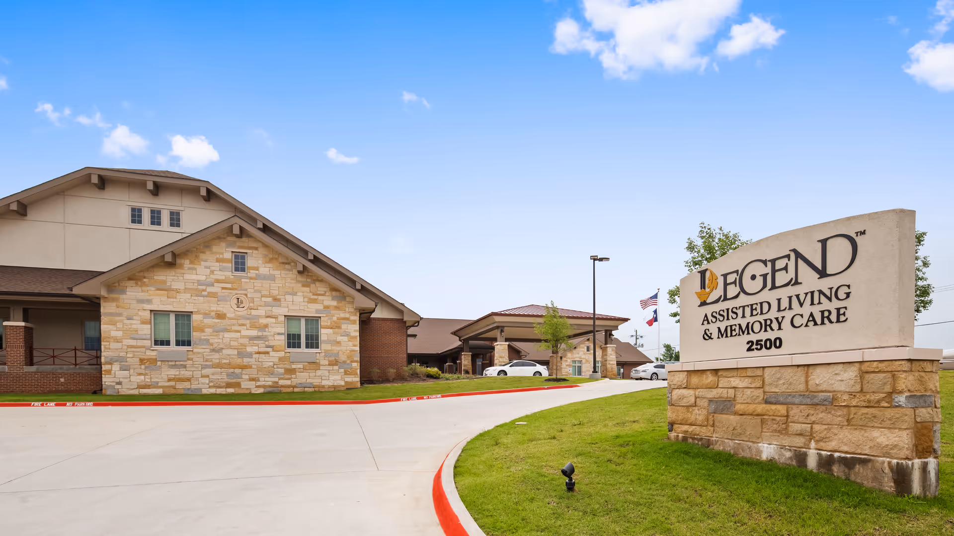 Exterior view of Legend Assisted Living building with stone signage and driveway curving.
