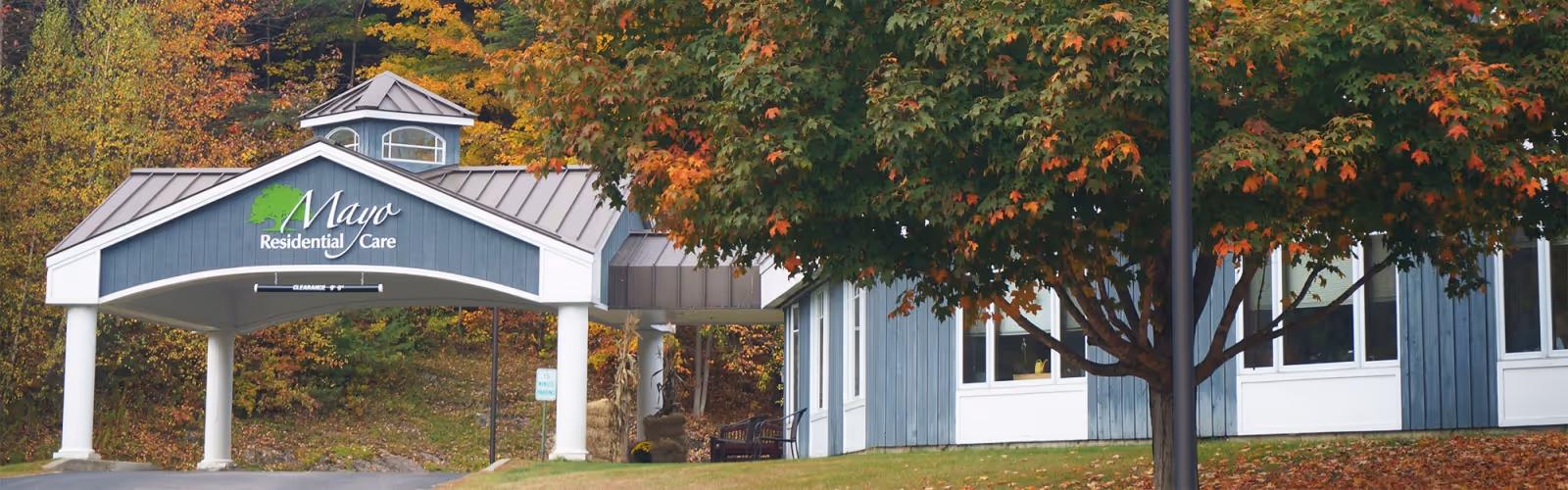 Exterior view of Mayo Residential Care facility with a covered entrance and autumn trees.