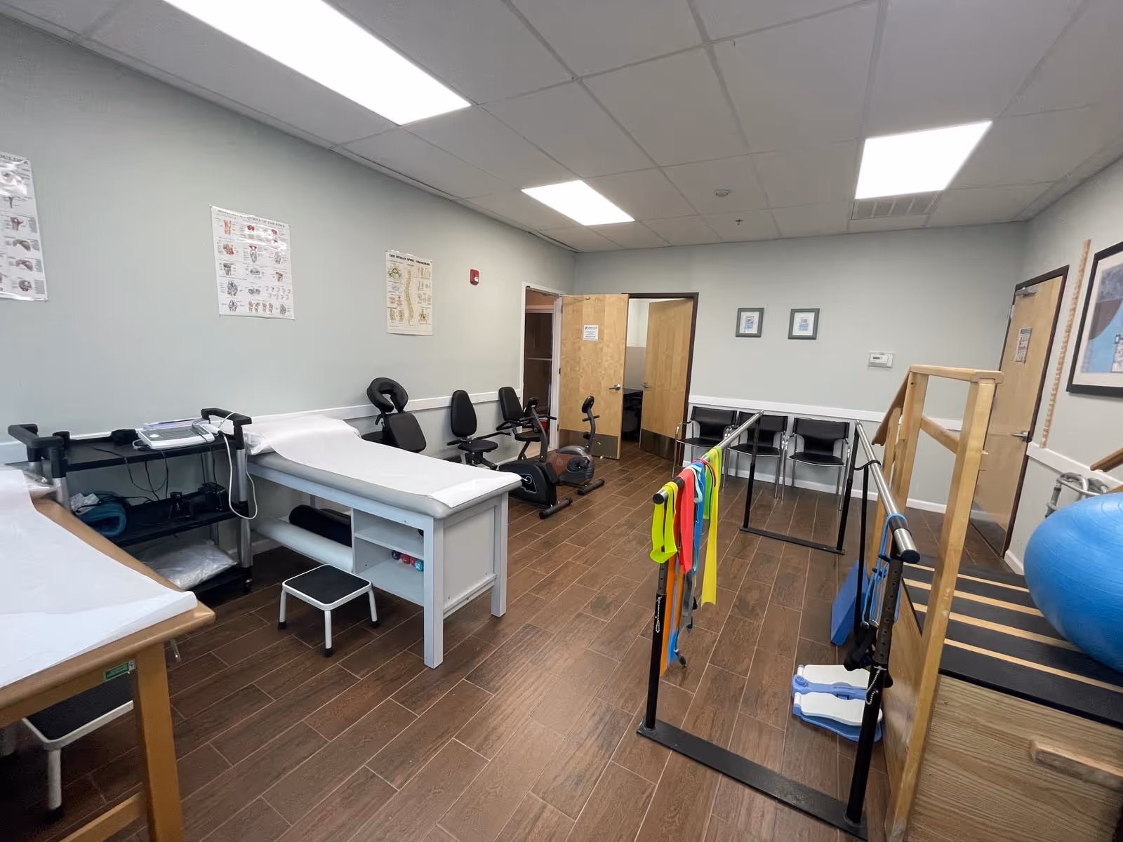 A rehabilitation room with treatment tables, exercise equipment, and parallel bars in a clinic.
