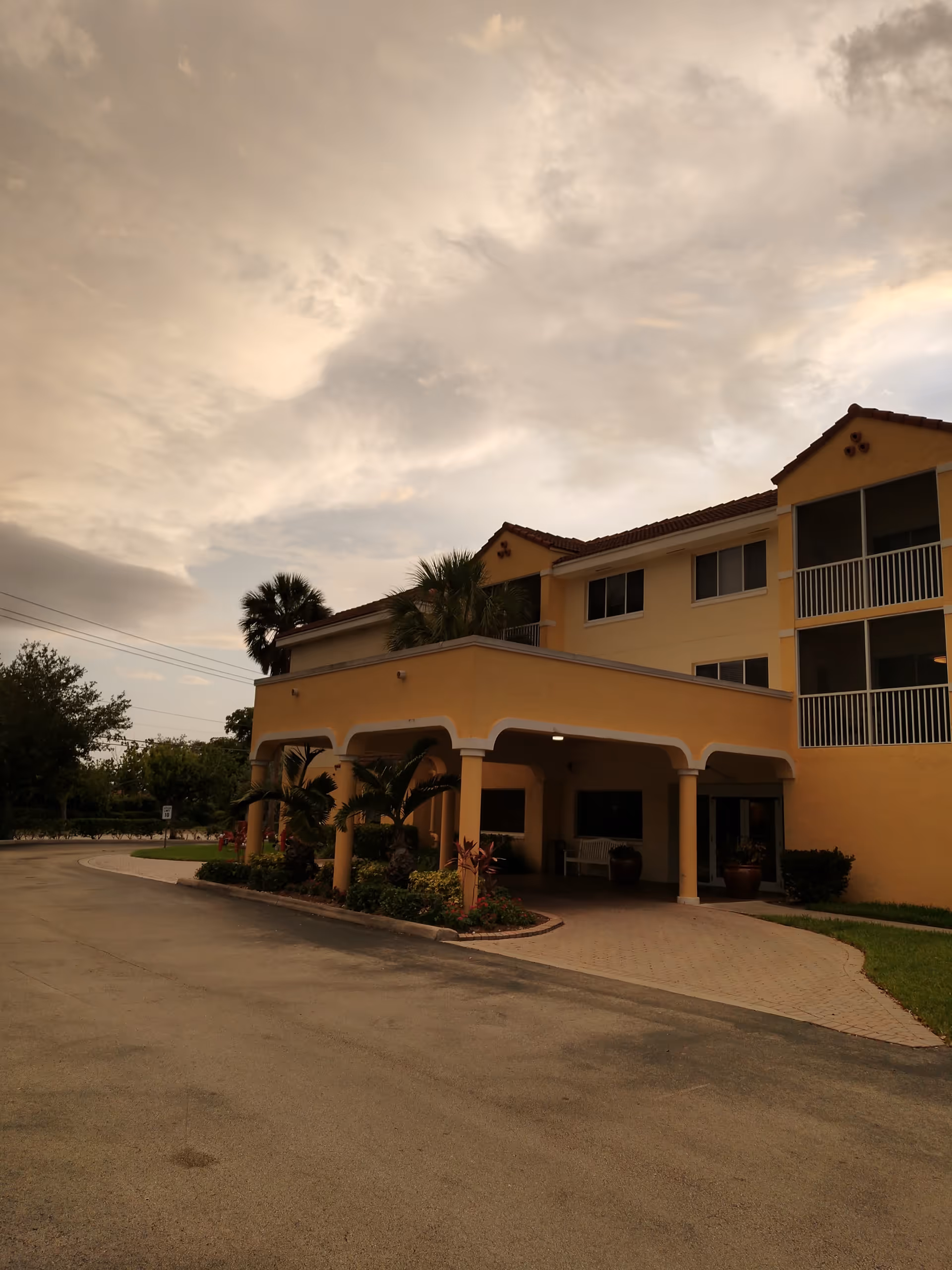 Three-story yellow senior living building with a covered entrance and palm landscaping.