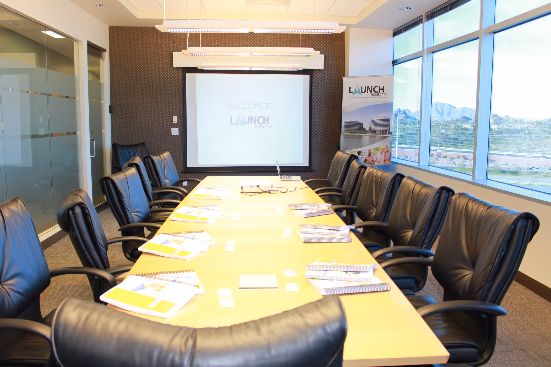 A conference room with a long table, black chairs, projector screen, and large windows.