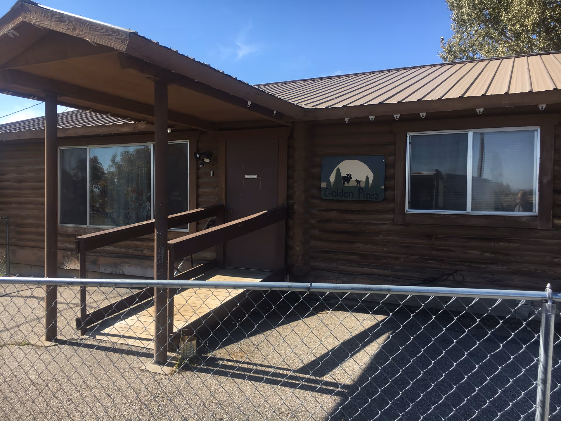 Log cabin-style facility exterior with ramp access, chain-link fence, and a Golden Pines sign.