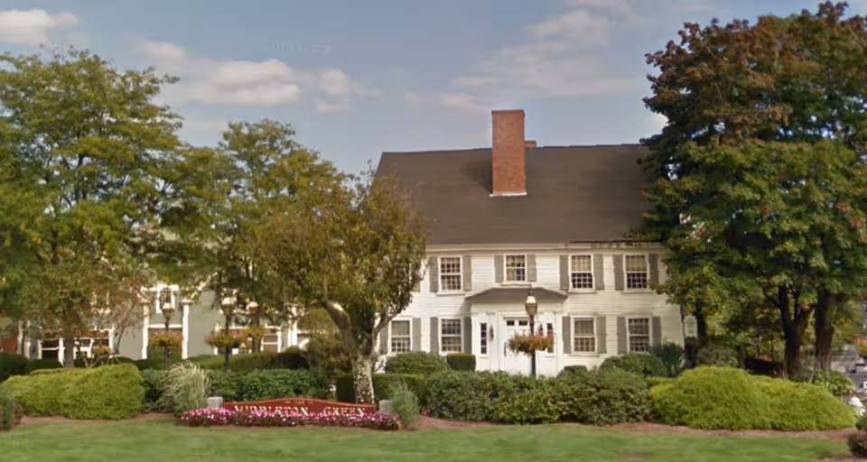 Front view of a white colonial-style senior care building with landscaped grounds.
