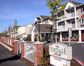 Front exterior of the Vintage Everett apartment building showing the entryway, sign, balconies, and brick fence.