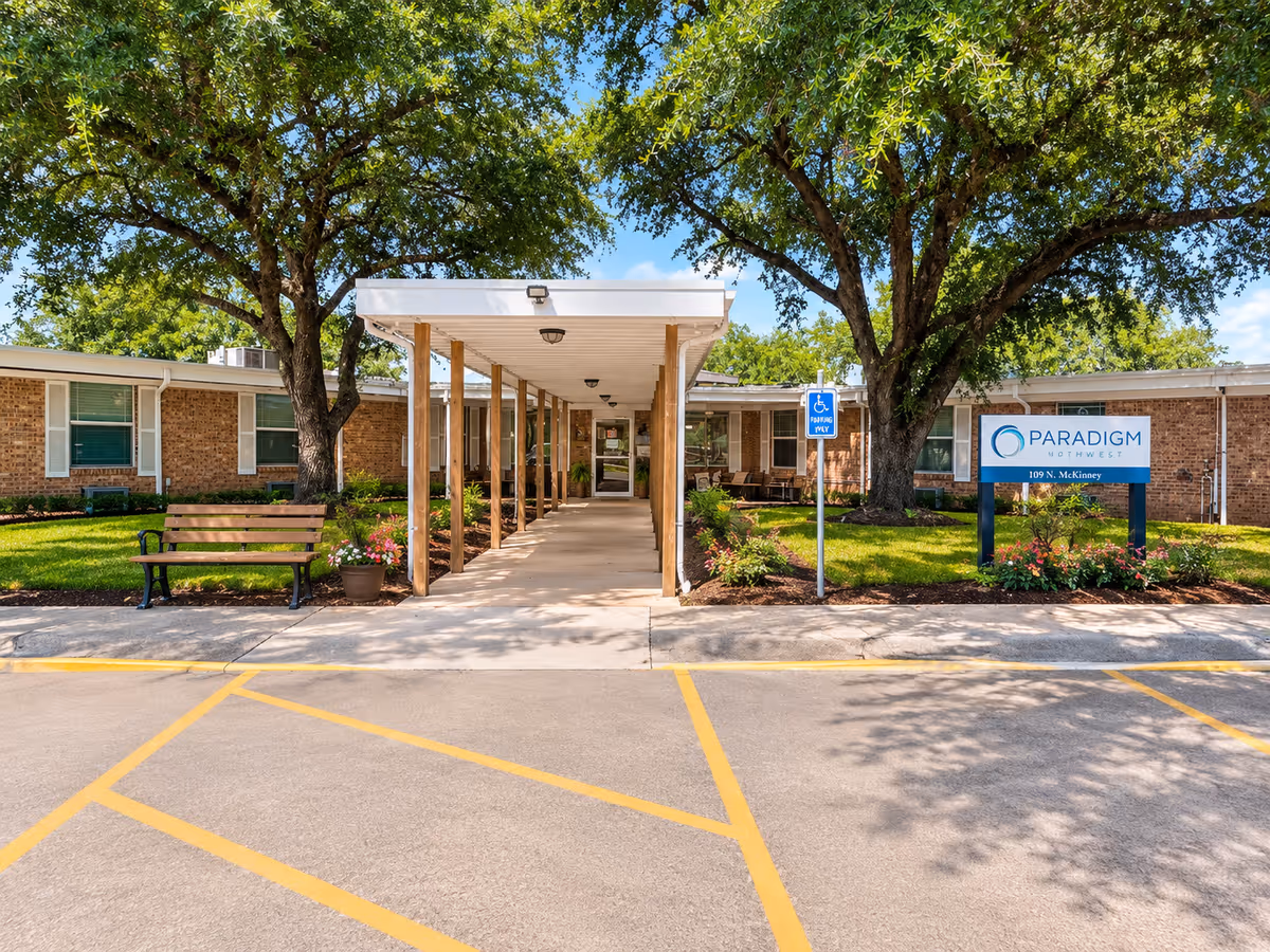 Exterior view of Sweeny House senior living entrance with a covered walkway and trees.