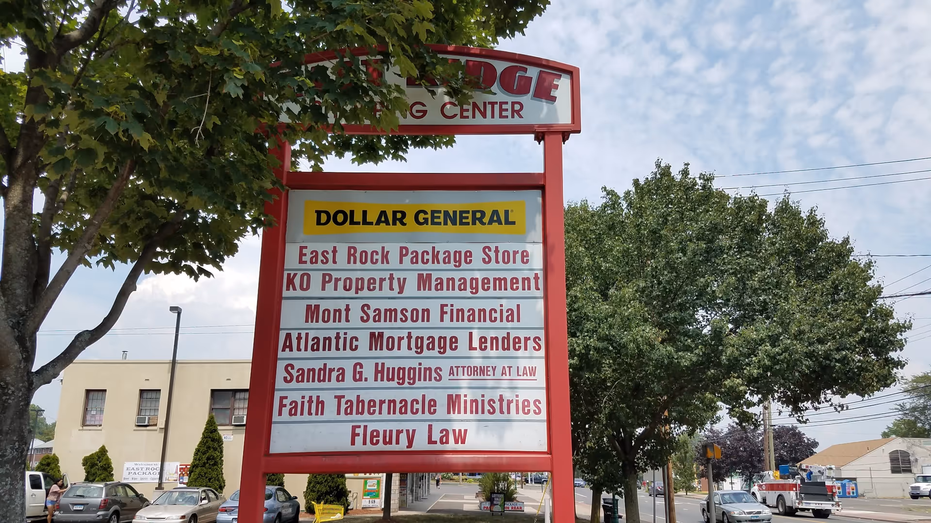 Tall red-framed outdoor signboard advertising Dollar General and nearby businesses on a street.
