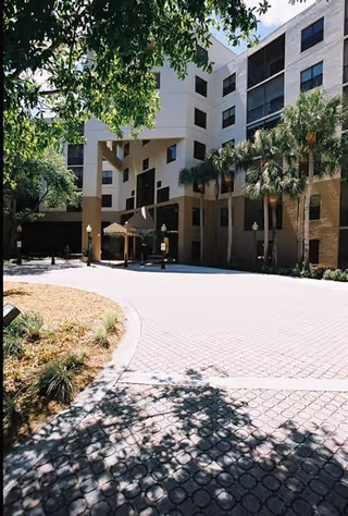 Exterior view of Brookdale Palm Beach Gardens with palm trees, entrance, and brick-paver driveway.
